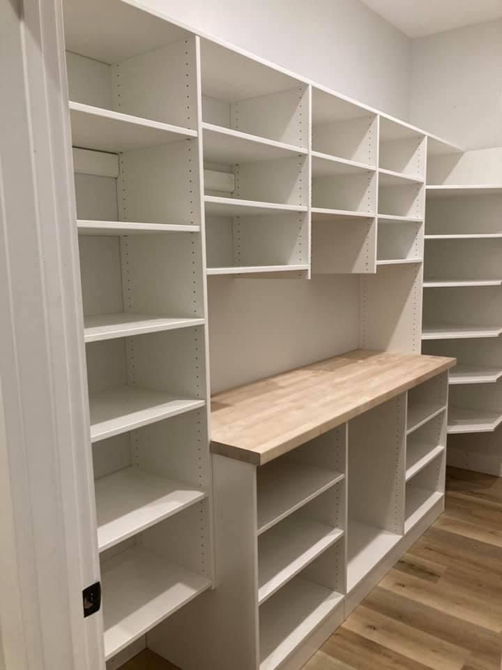 White pantry shelving with butcher block countertop and light wood flooring.