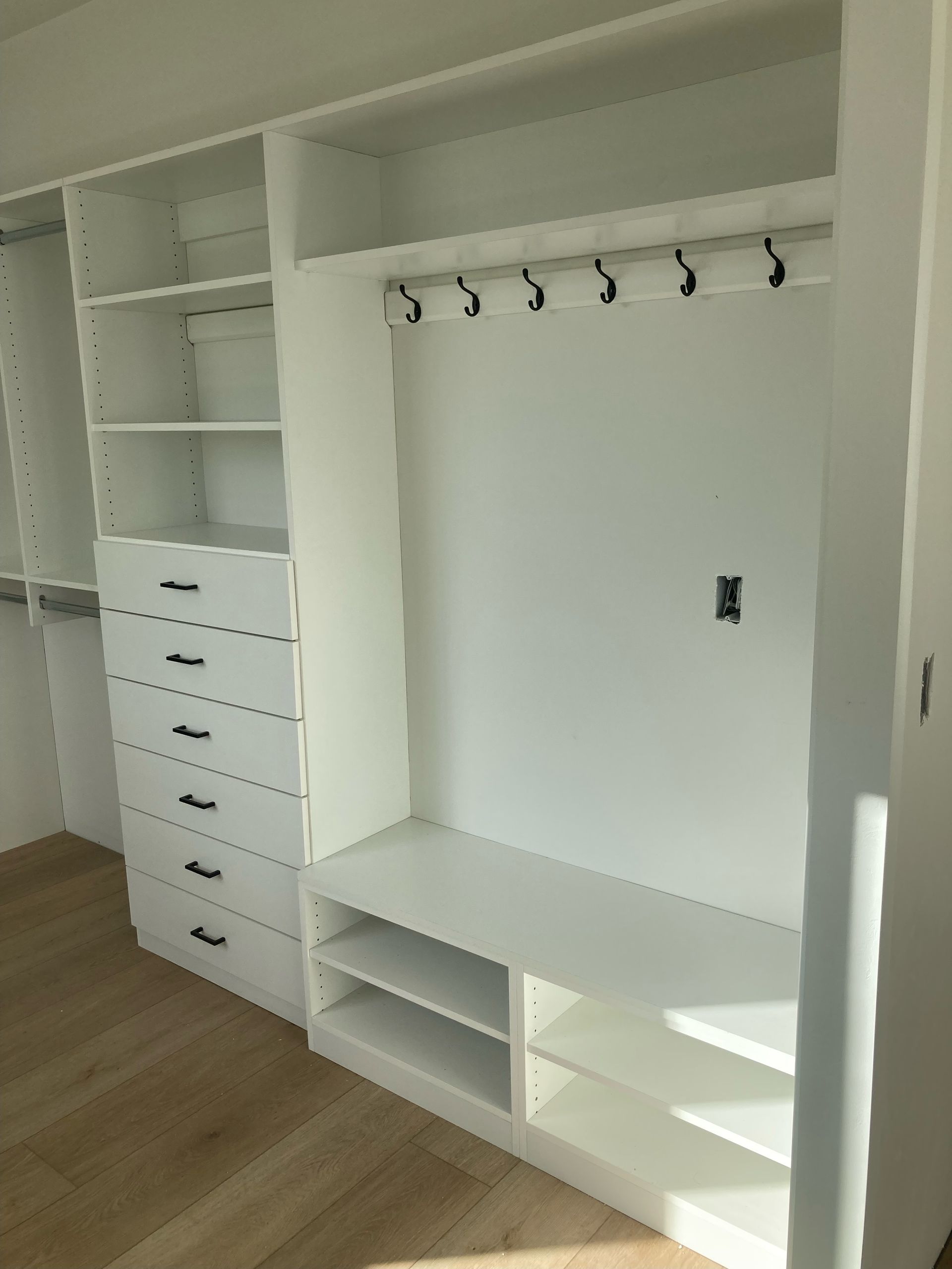 White custom closet with drawers, shelving, hanging rods, and a bench.