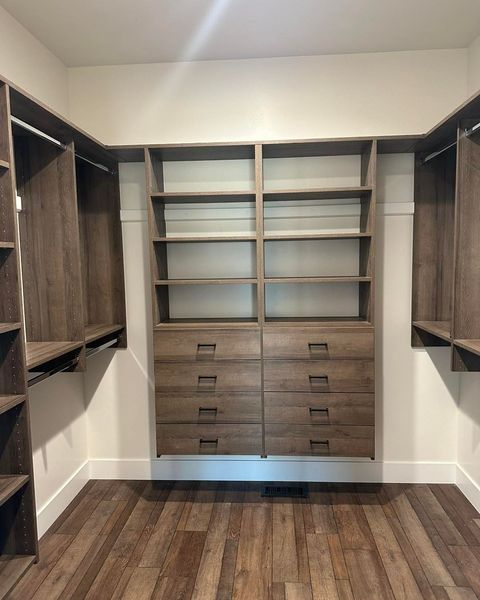 Empty walk-in closet with wood shelves, drawers, and flooring against white walls.