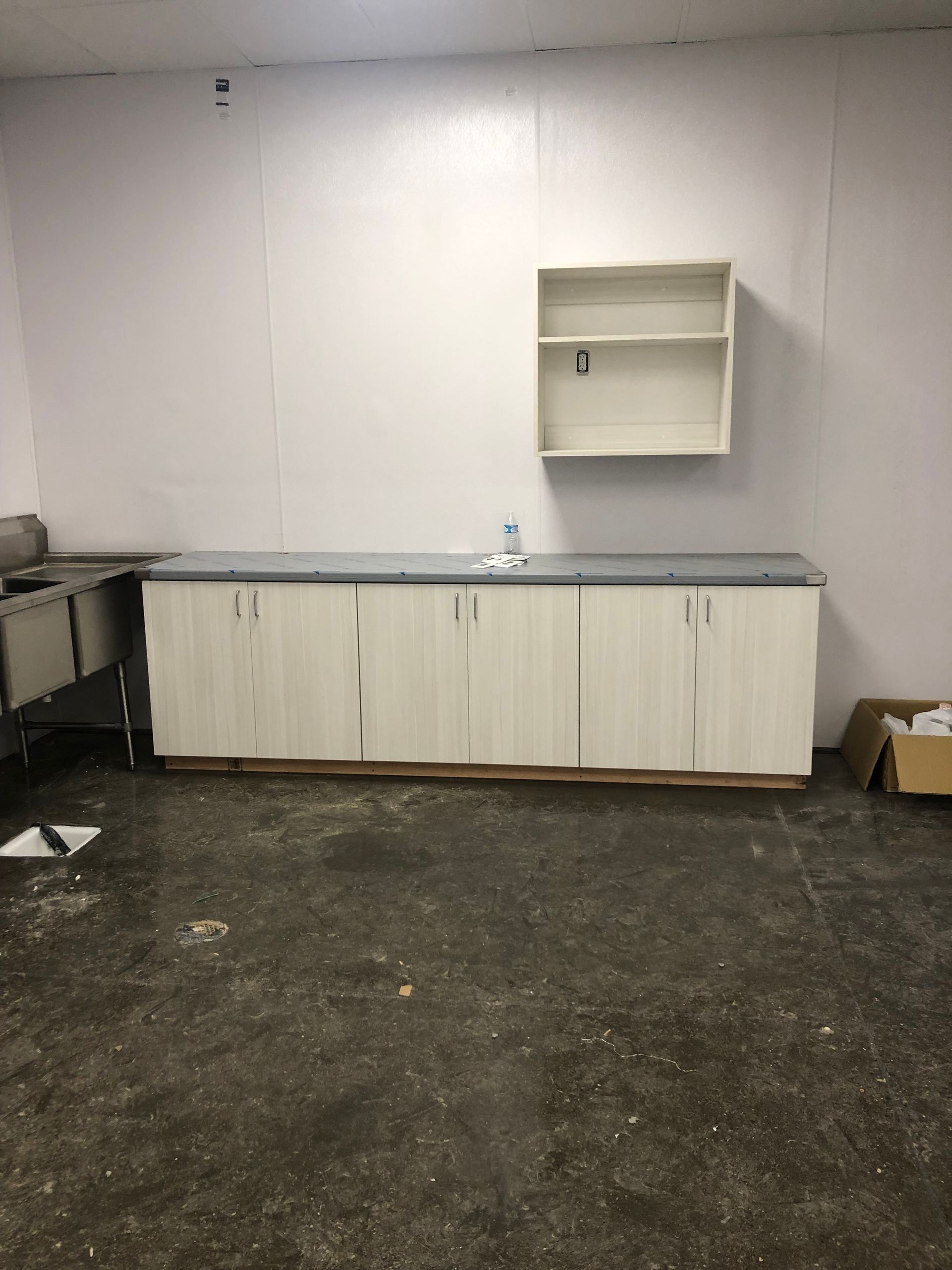 Kitchen cabinets and shelf against a white wall in a room with a dirty floor.