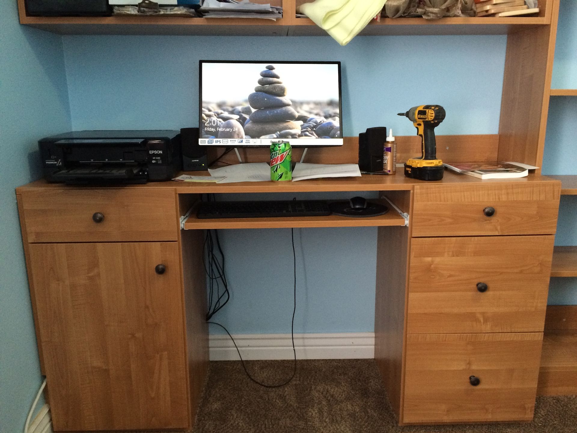 Wooden desk with computer, printer, and tools against a blue wall.