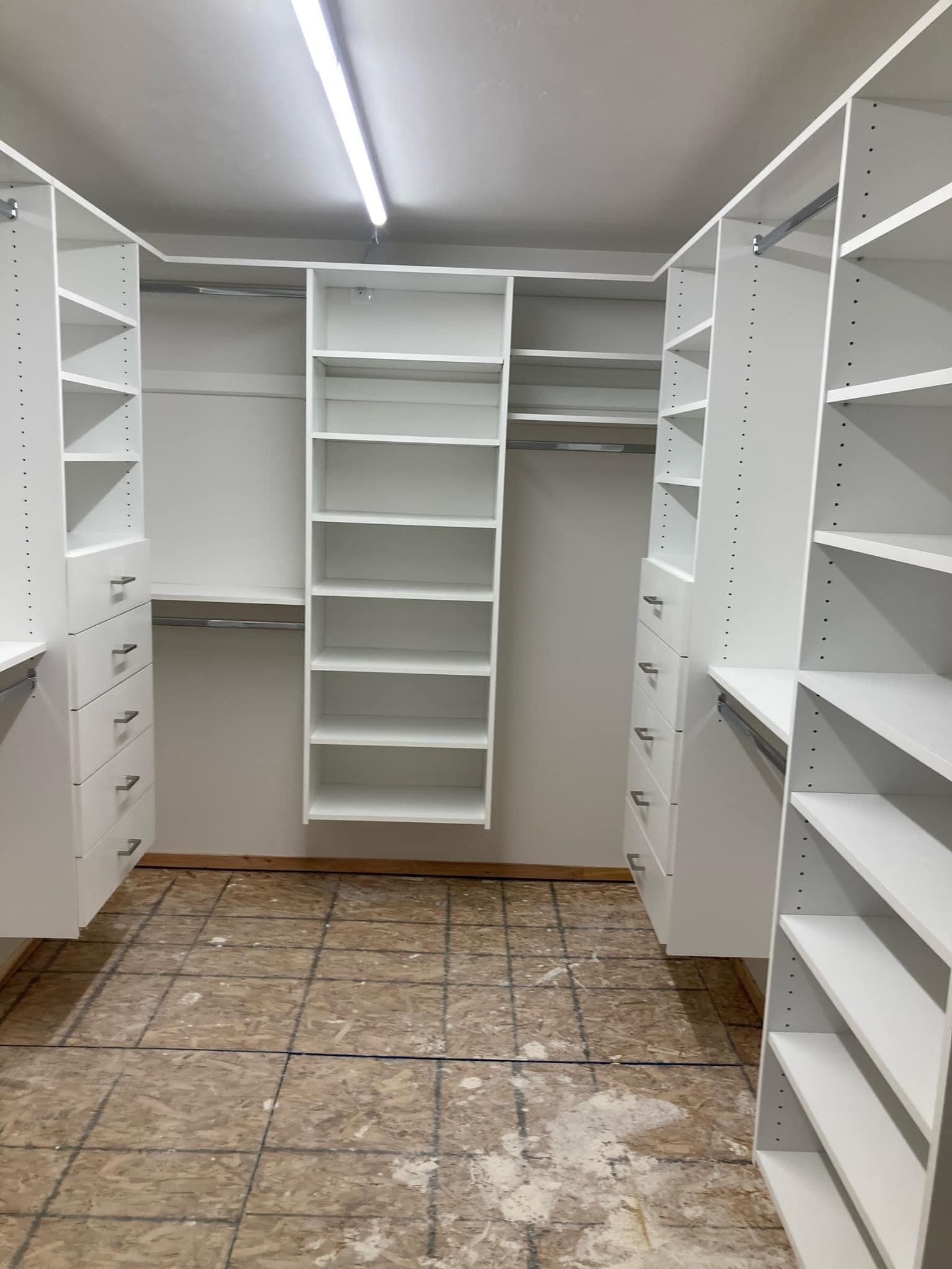 White walk-in closet with shelves, drawers, and hanging rods, awaiting flooring.