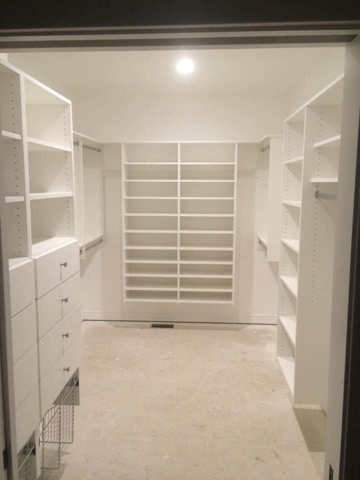 Empty white walk-in closet with shelves, drawers, and hanging rods.