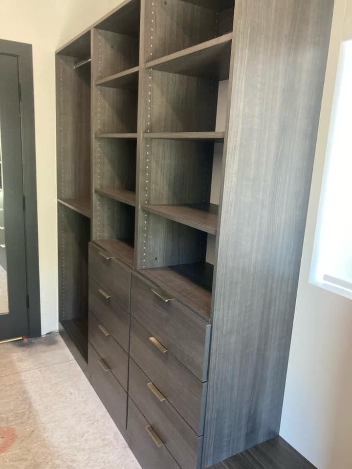 Custom gray wooden closet system with shelves and drawers in a room.