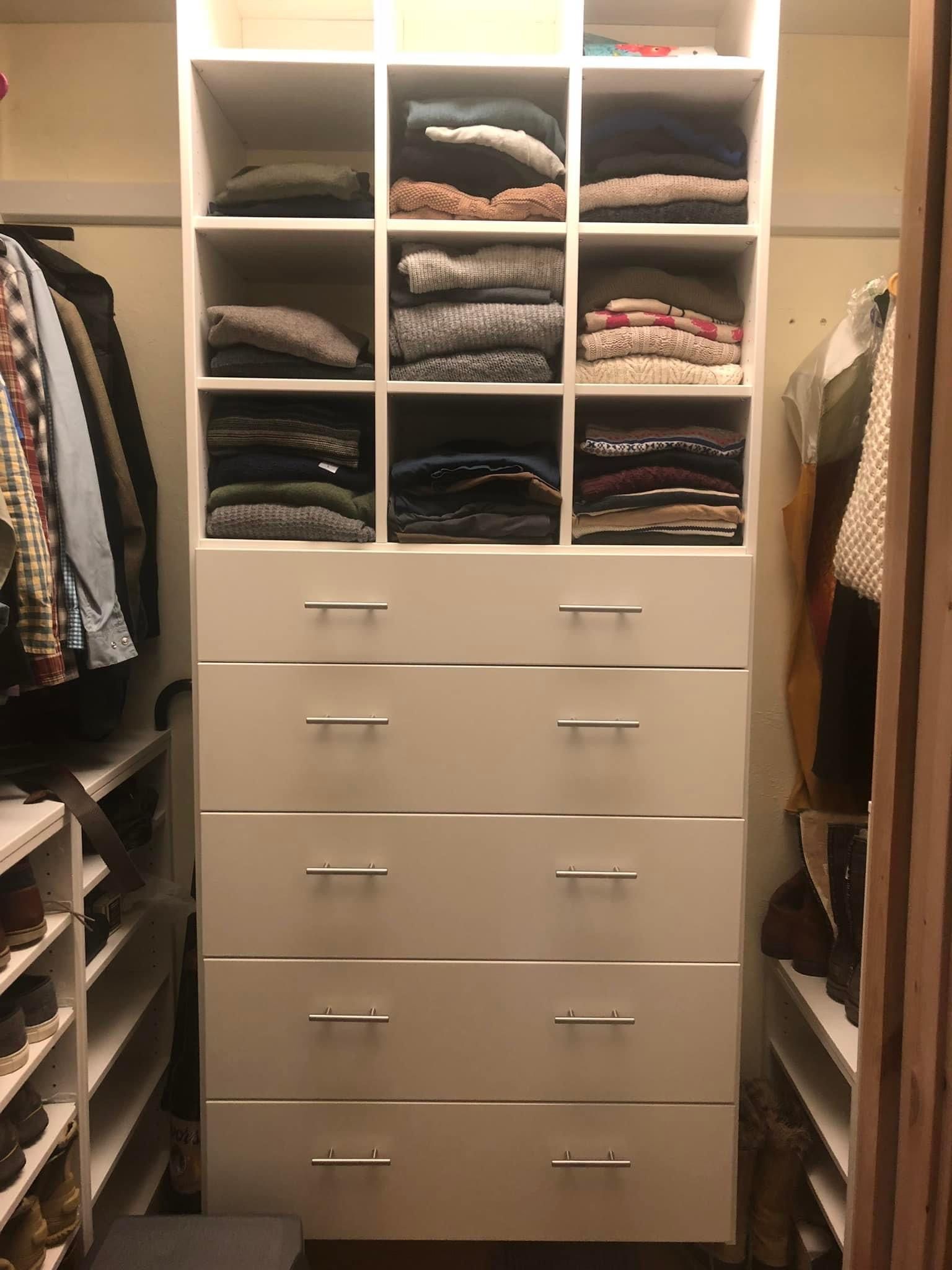 White closet with shelves of folded clothes above five drawers.