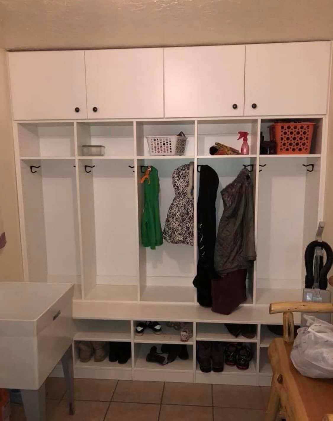 White built-in entryway storage with upper cabinets, hooks, shoe cubbies, and hanging clothes.