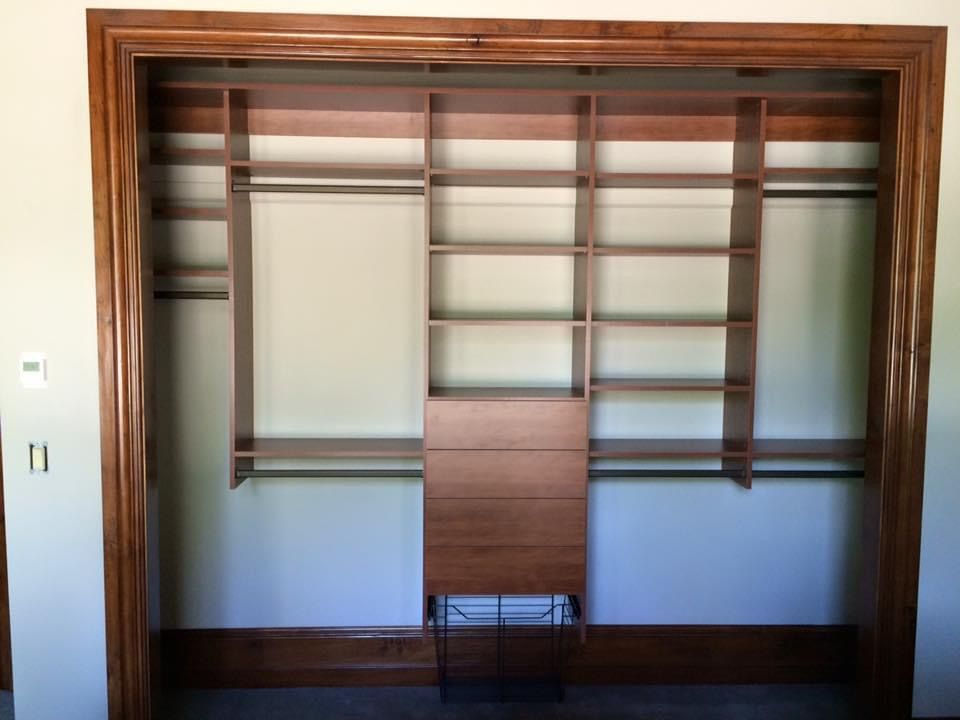 Built-in wooden closet with shelves, hanging rods, and a center cabinet, all in a light brown color.