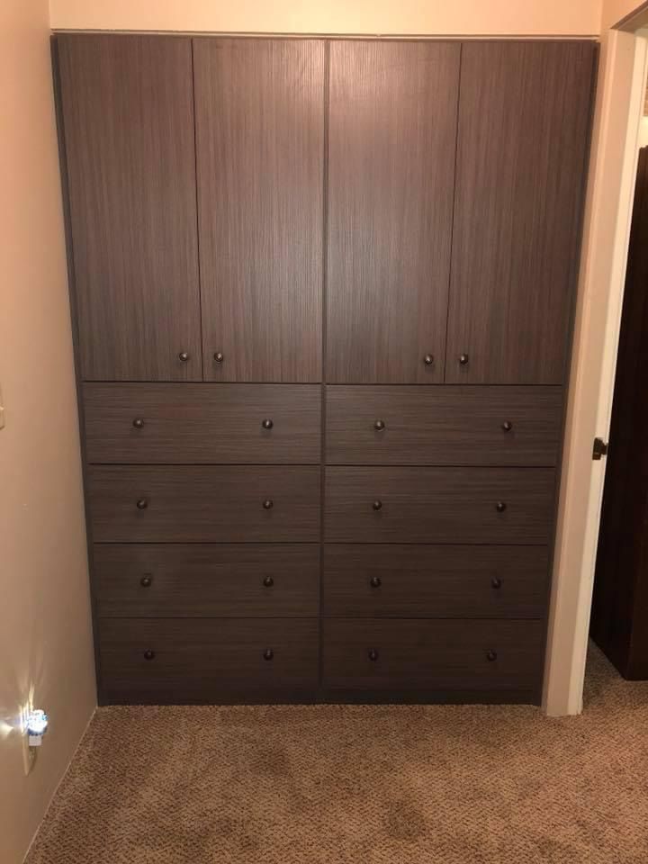 Dark wood closet with upper cabinets and lower drawers in a bedroom.