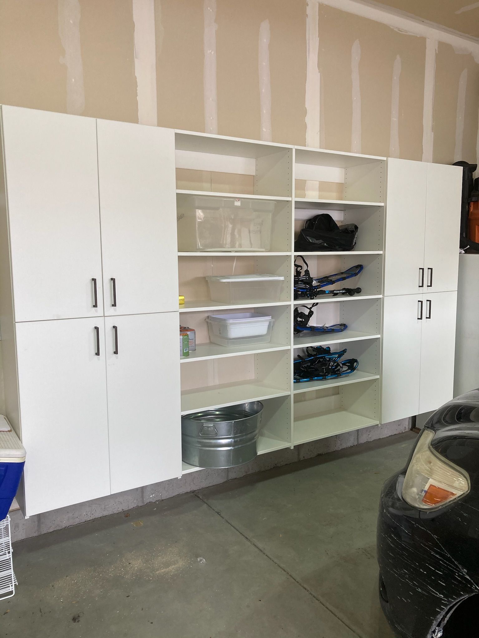 White garage storage cabinets with shelves and doors, partially filled with items, mounted on a wall.