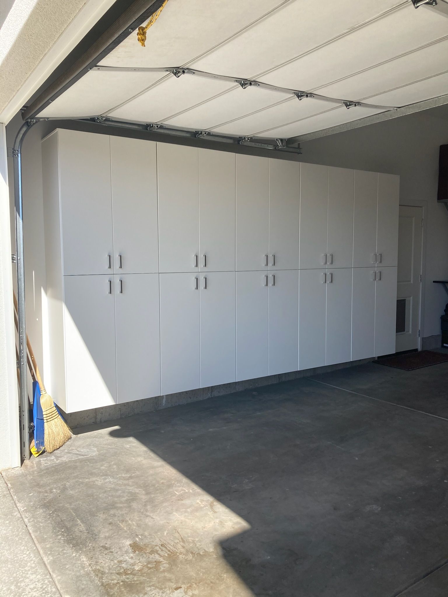 White storage cabinets in a garage, with gray concrete floor and garage door open.
