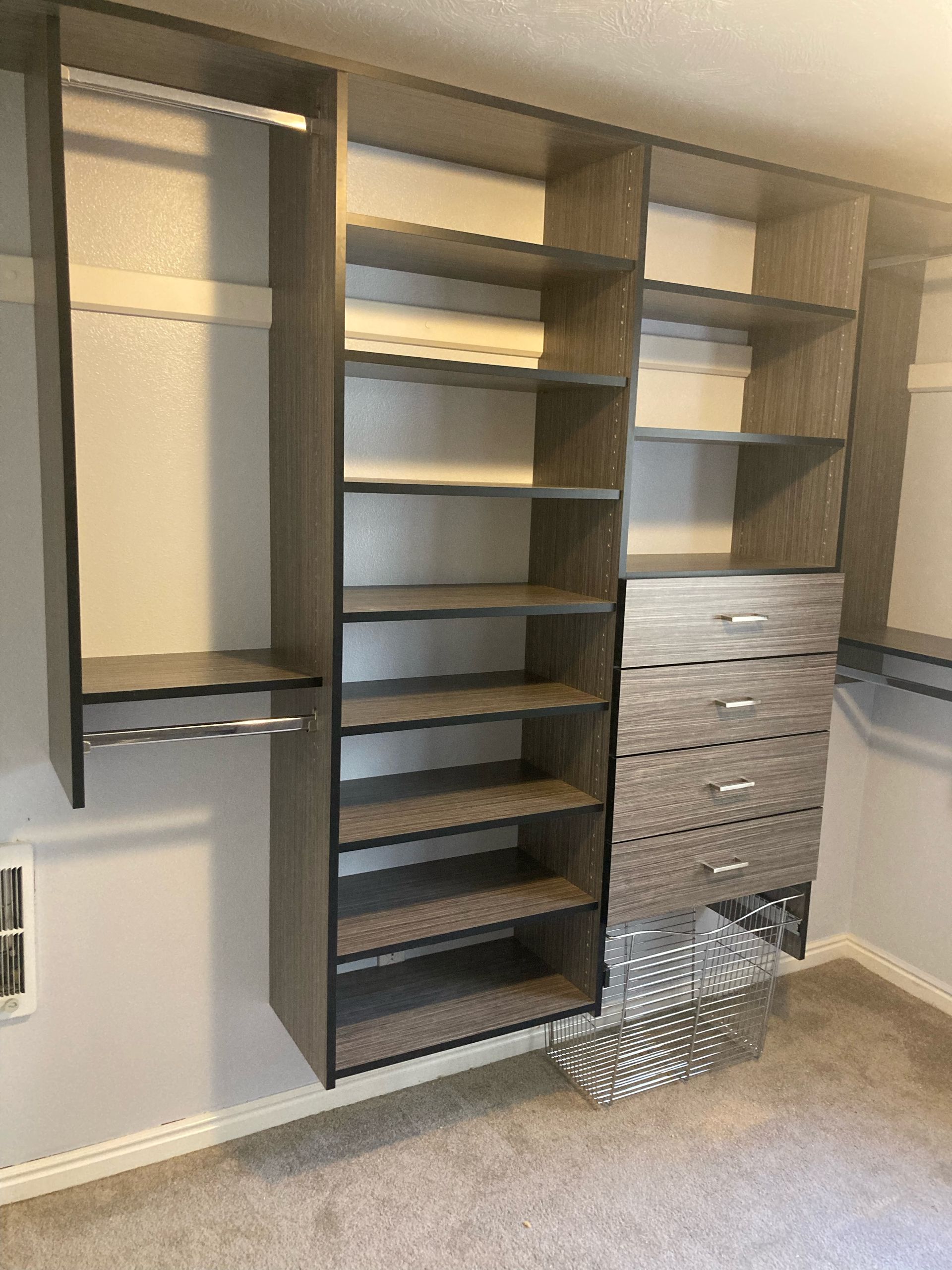 Gray closet organizer with shelves, drawers, and hanging rod in a room with carpet.