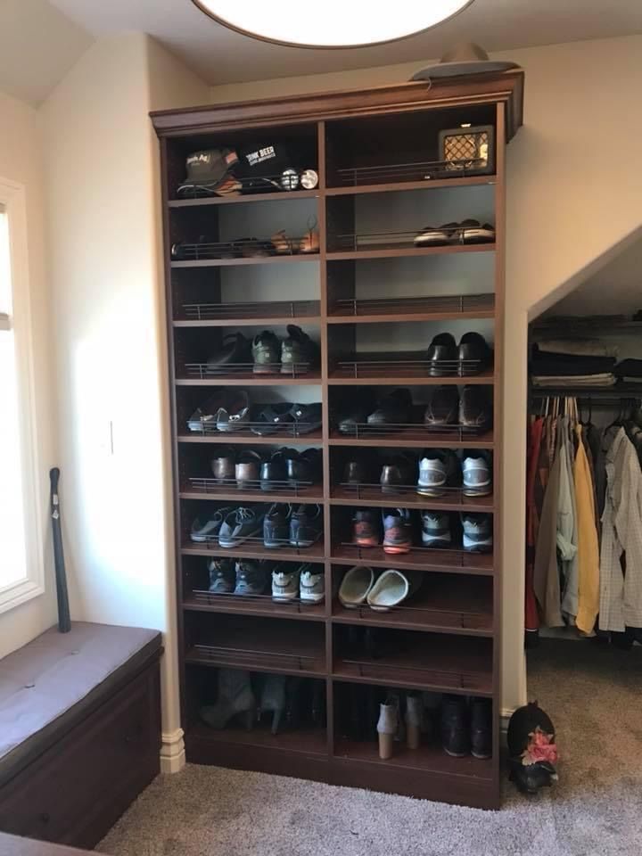 Tall wooden shoe storage unit filled with shoes, in a room next to a closet.