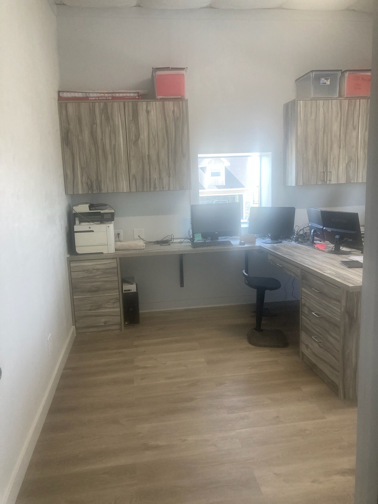 Office space with light wood cabinets, desk, computers, and printer; beige floor.