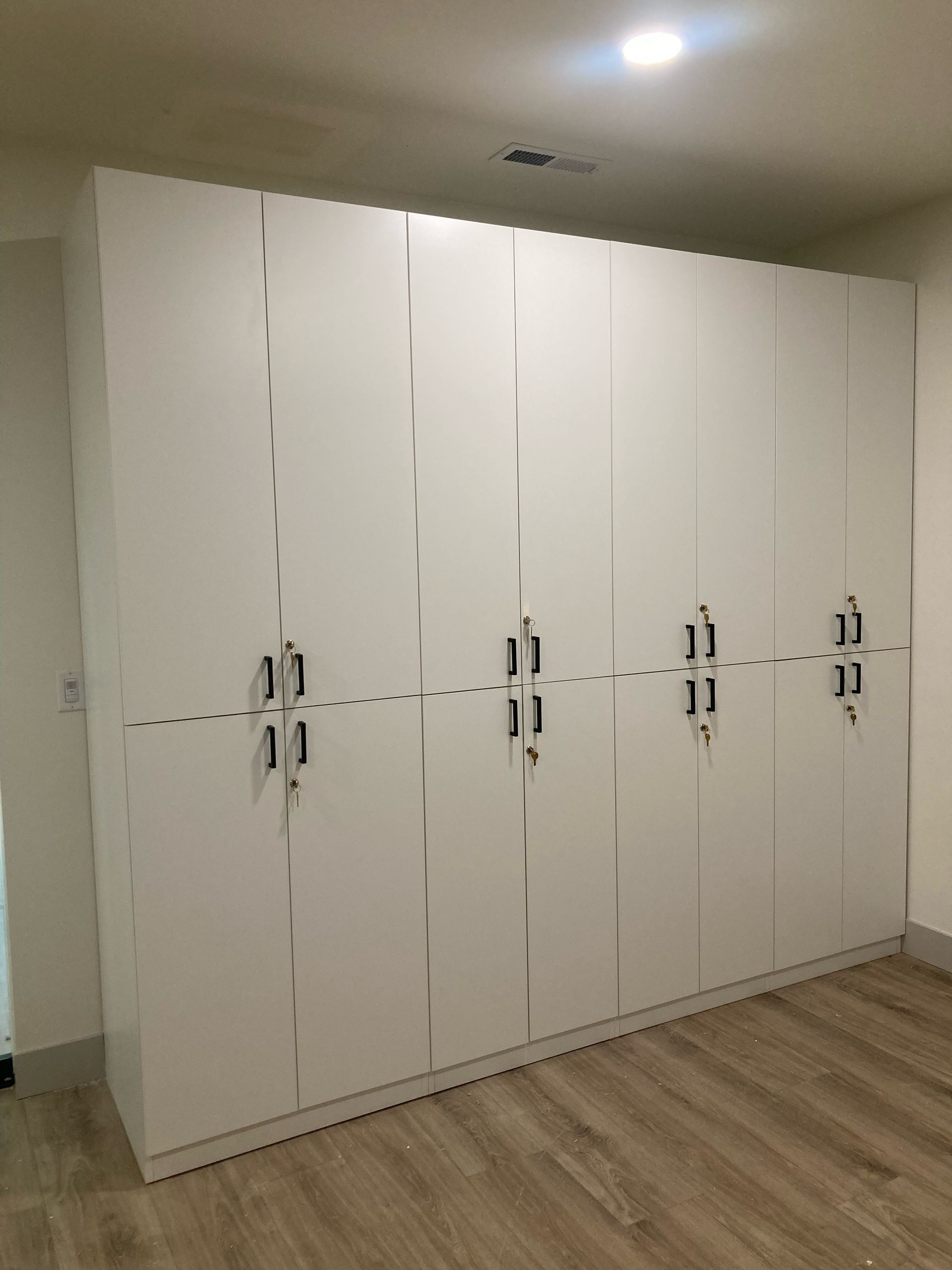 White closet doors in a room with wood-look flooring. Six sets of double doors with silver handles.