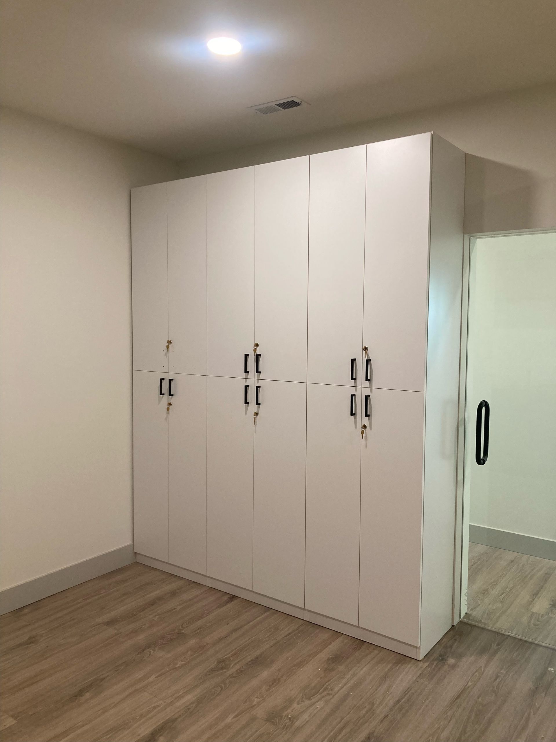 White built-in closet with dark handles in a room with wood floors and a doorway.
