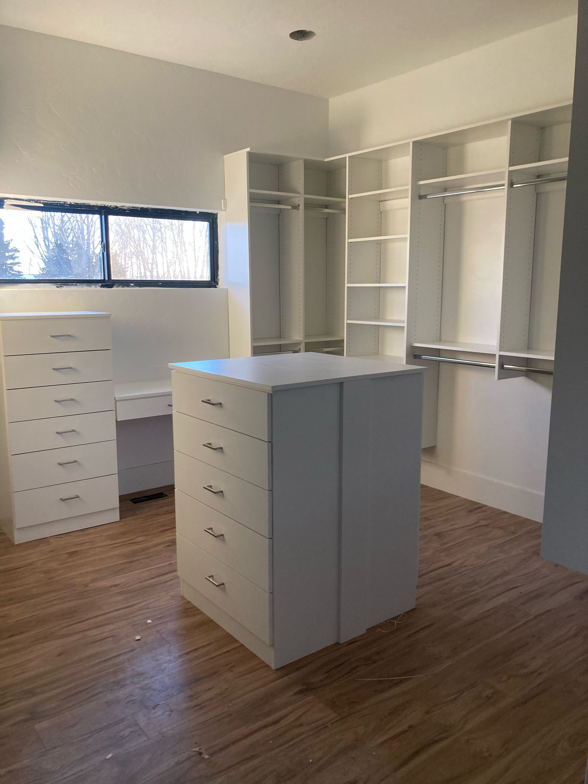 Empty white walk-in closet with built-in shelves, drawers, and a central island on wood flooring.