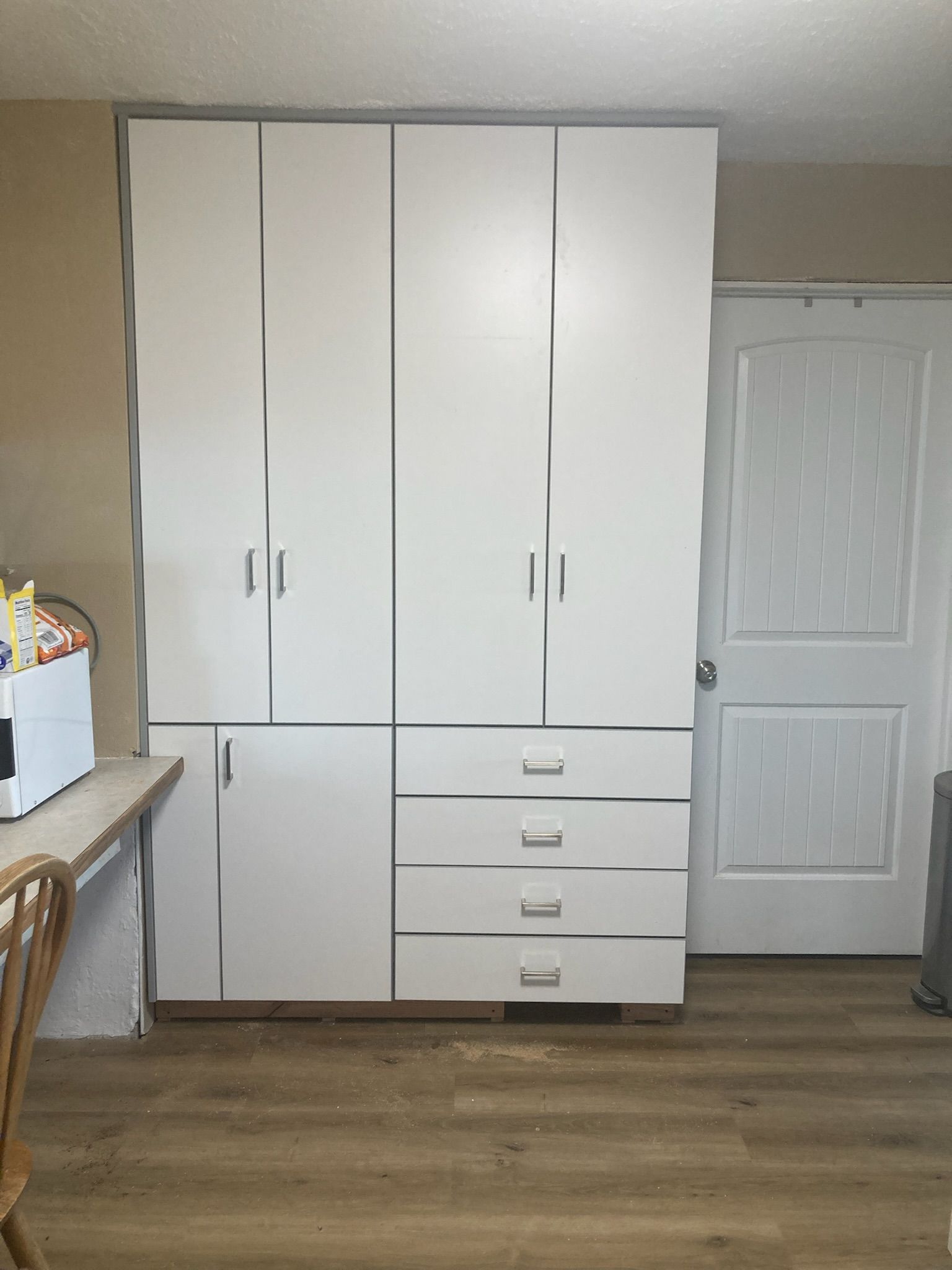 White storage cabinets with drawers against a beige wall. A white door is on the right.