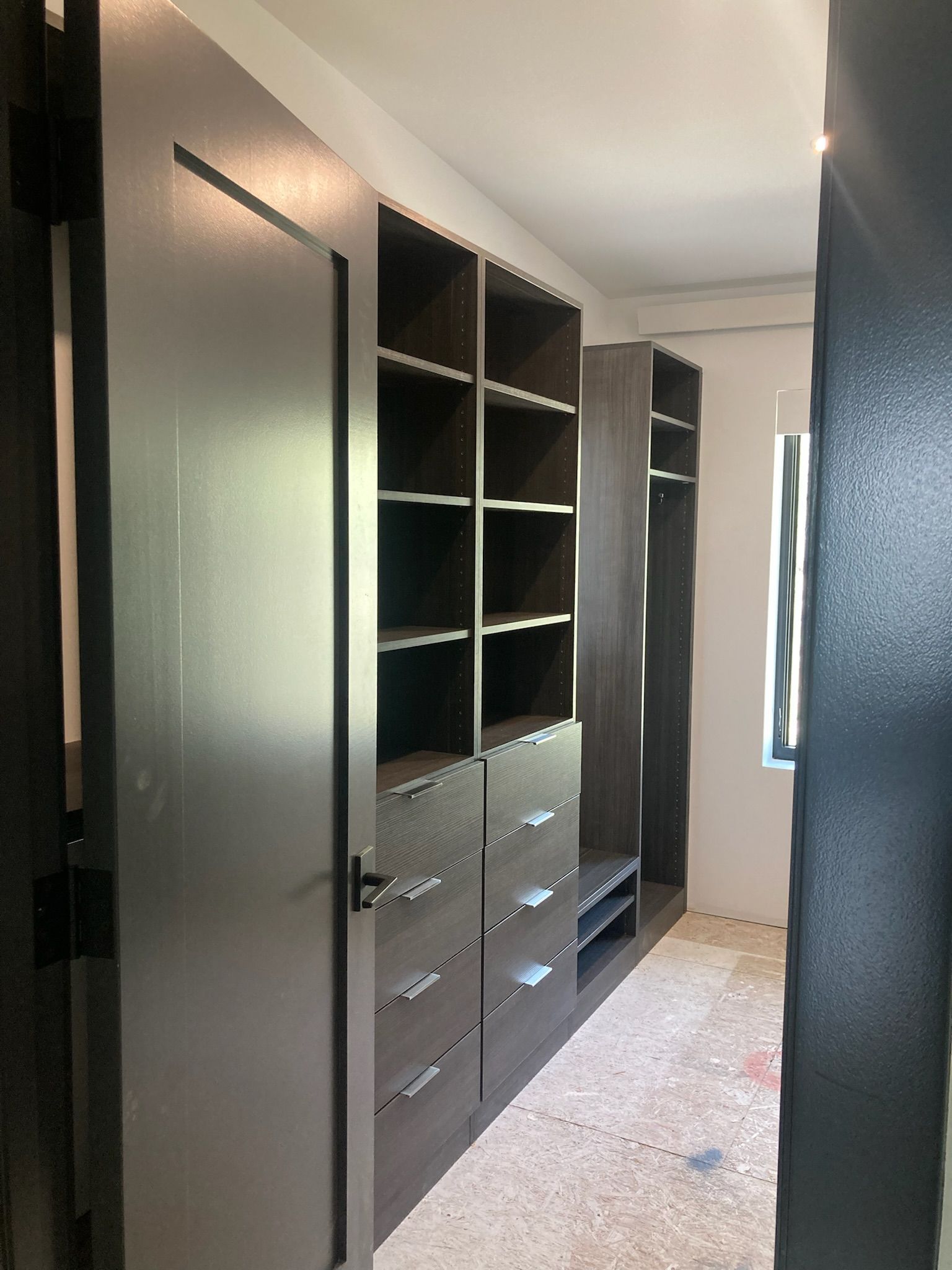 Walk-in closet with dark gray shelving, drawers, and a door. The space is still under construction.