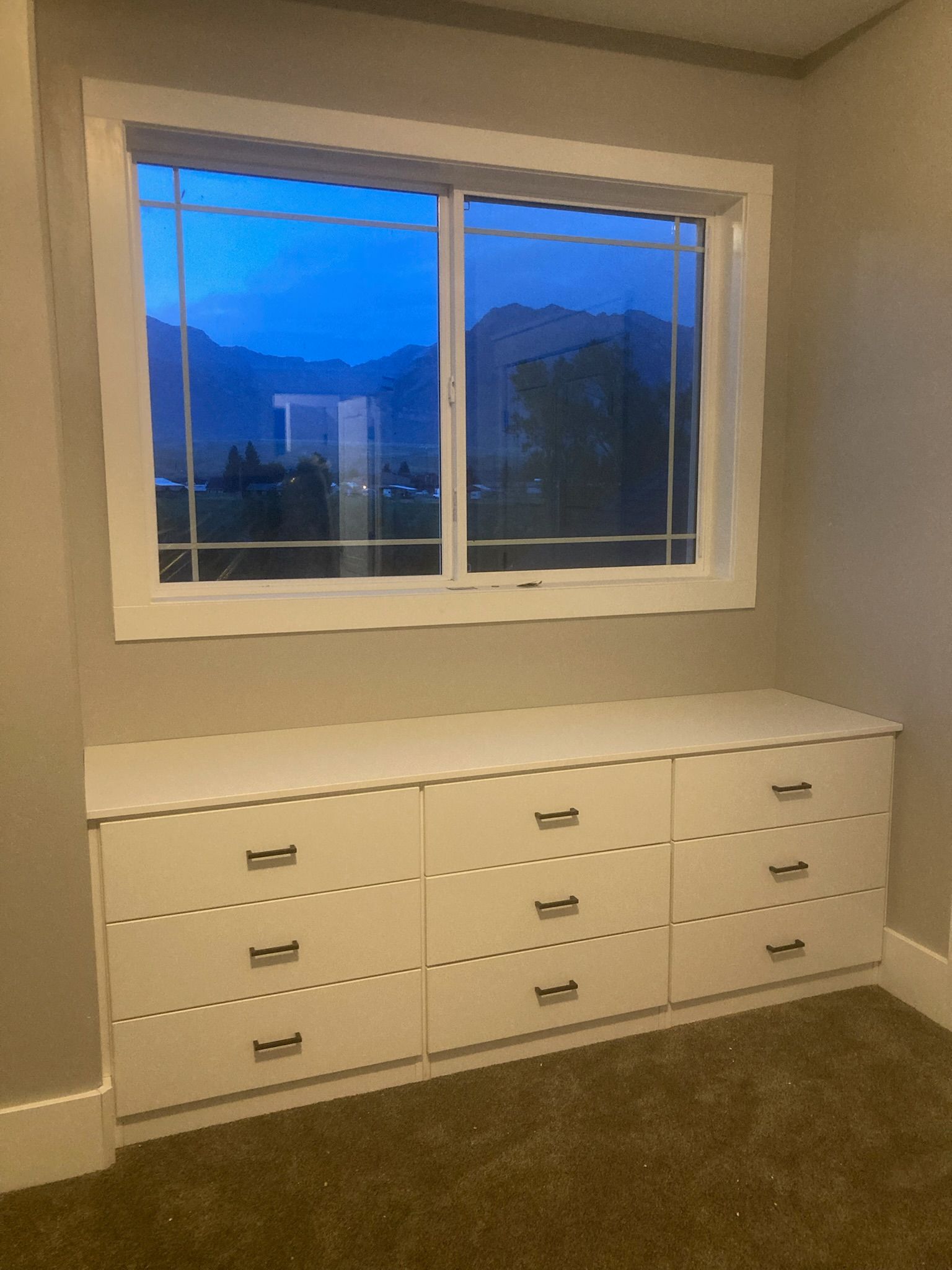 White dresser under a window with a mountain view; evening light.