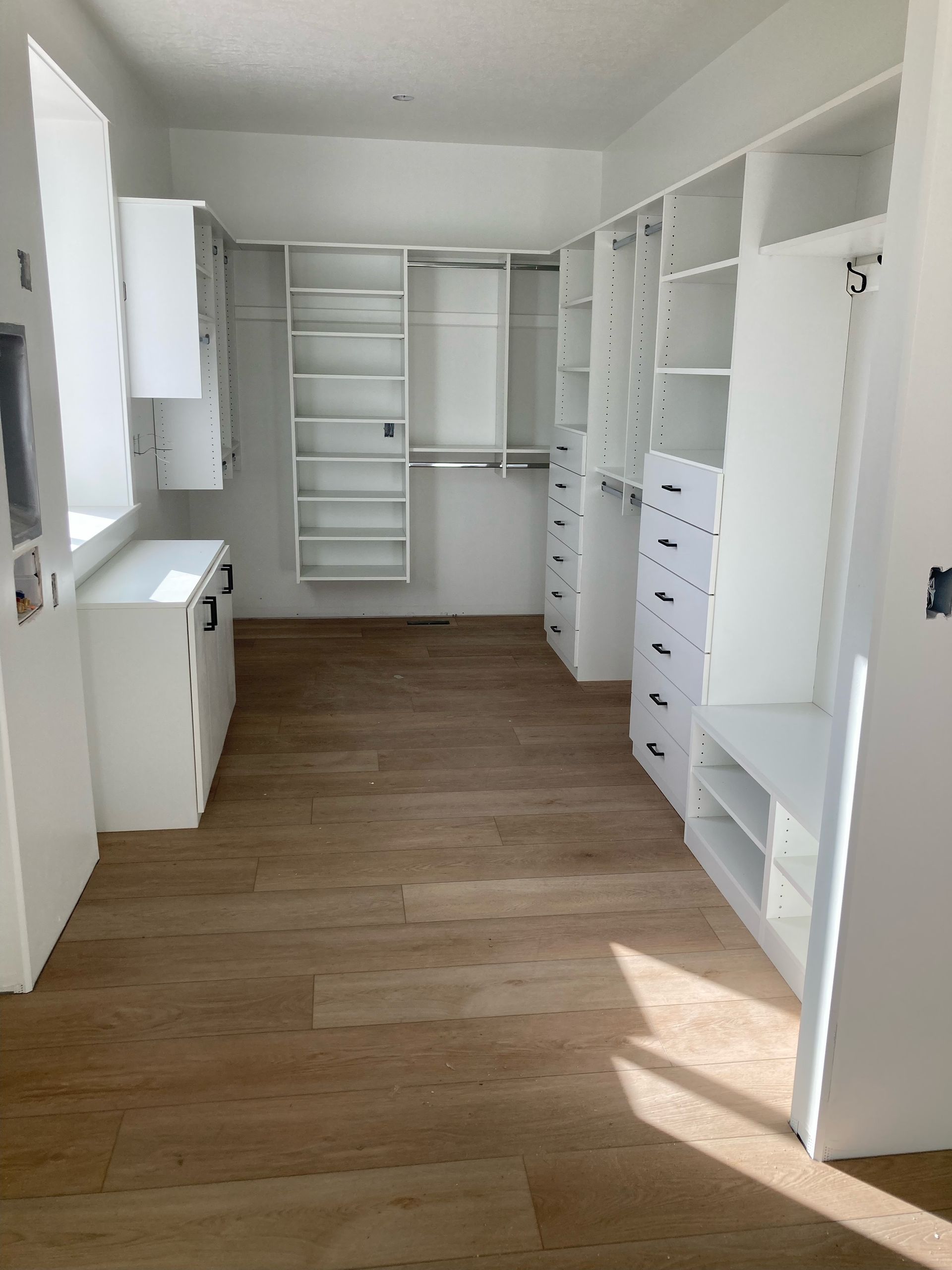 Empty white walk-in closet with wooden floor and built-in shelving and storage.