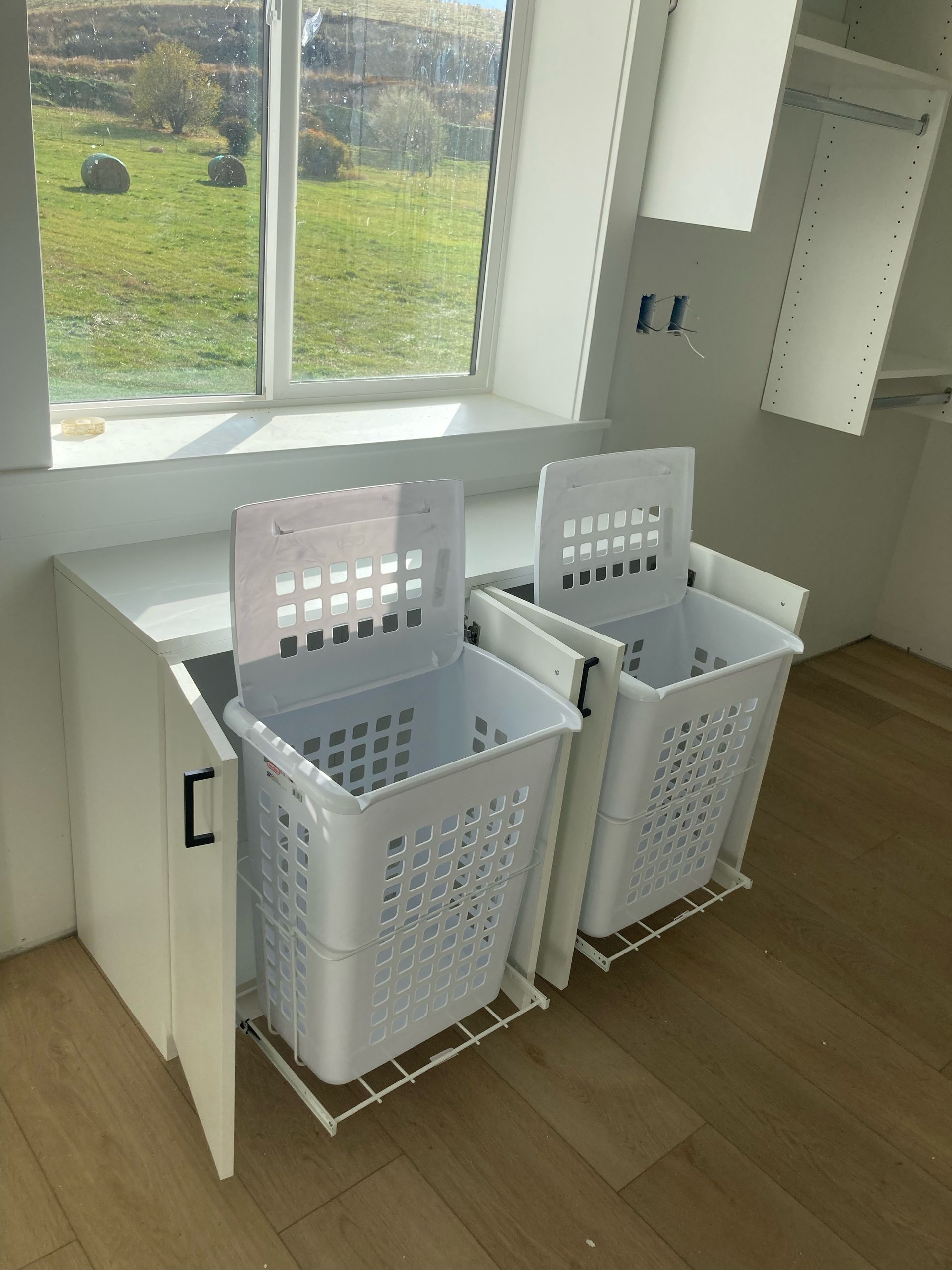 Laundry hamper system with white baskets, inside white cabinet, near a window.
