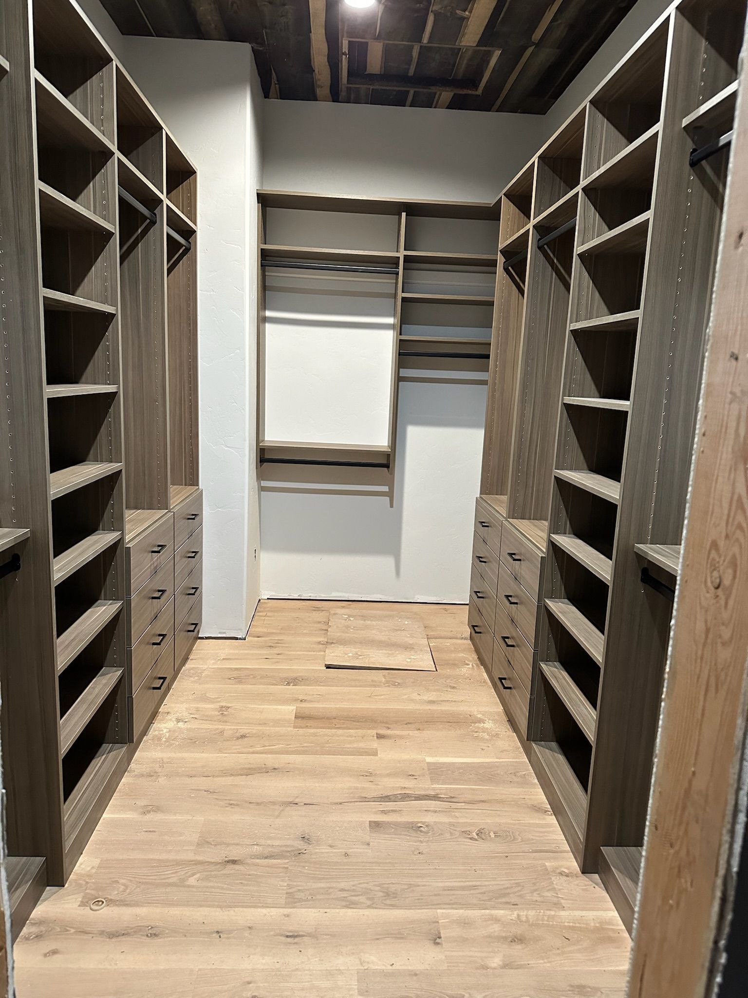 Spacious walk-in closet with wooden shelving and drawers on both sides; light wood floor, neutral walls.