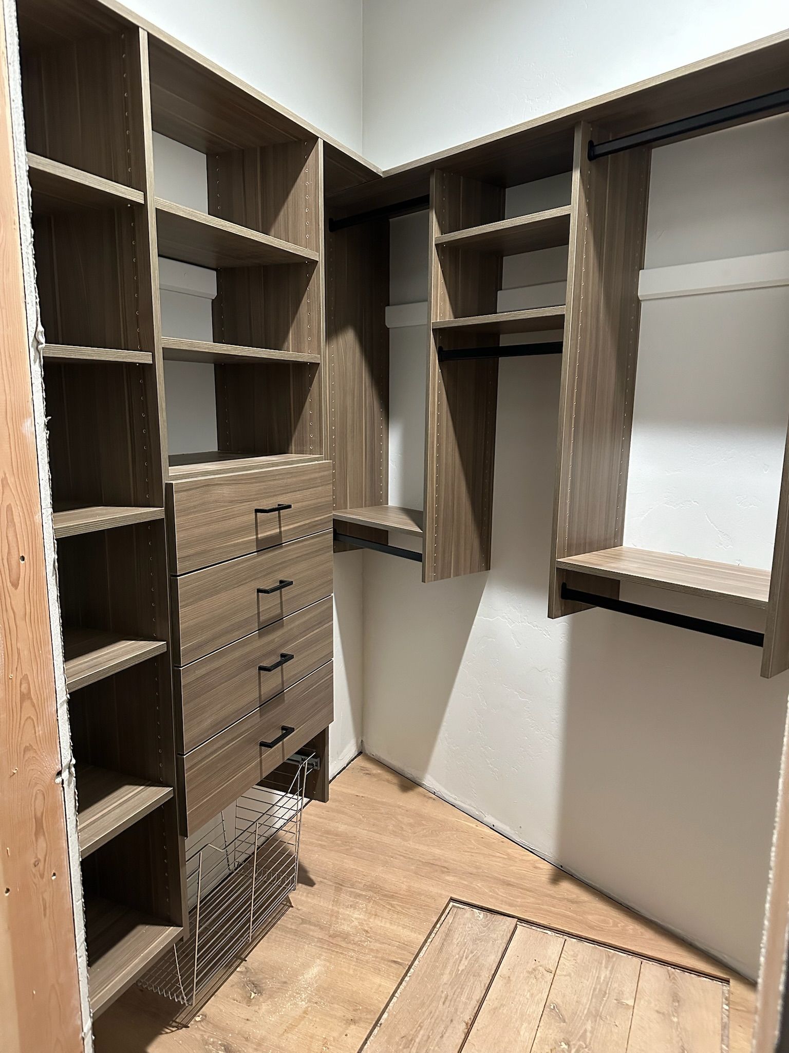 Wooden built-in closet with shelves, drawers, and hanging rods, in an unfinished room.