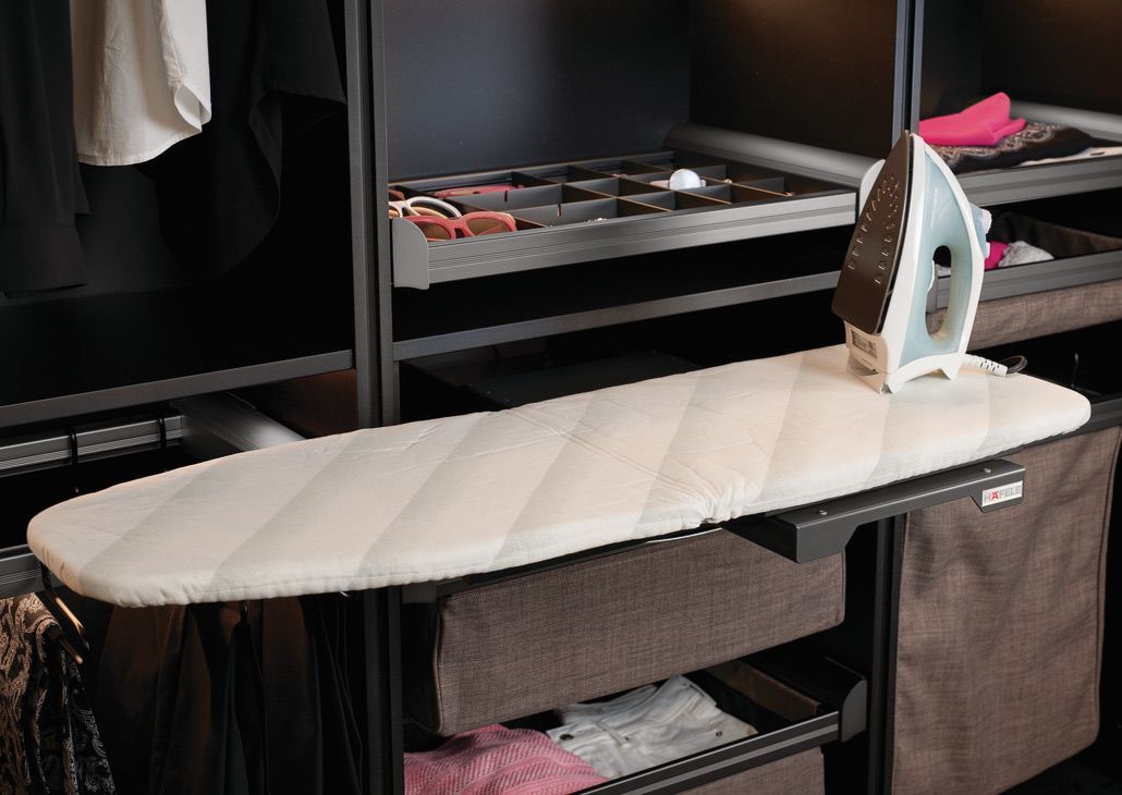 An ironing board with an iron, in a closet with shelving and drawers.
