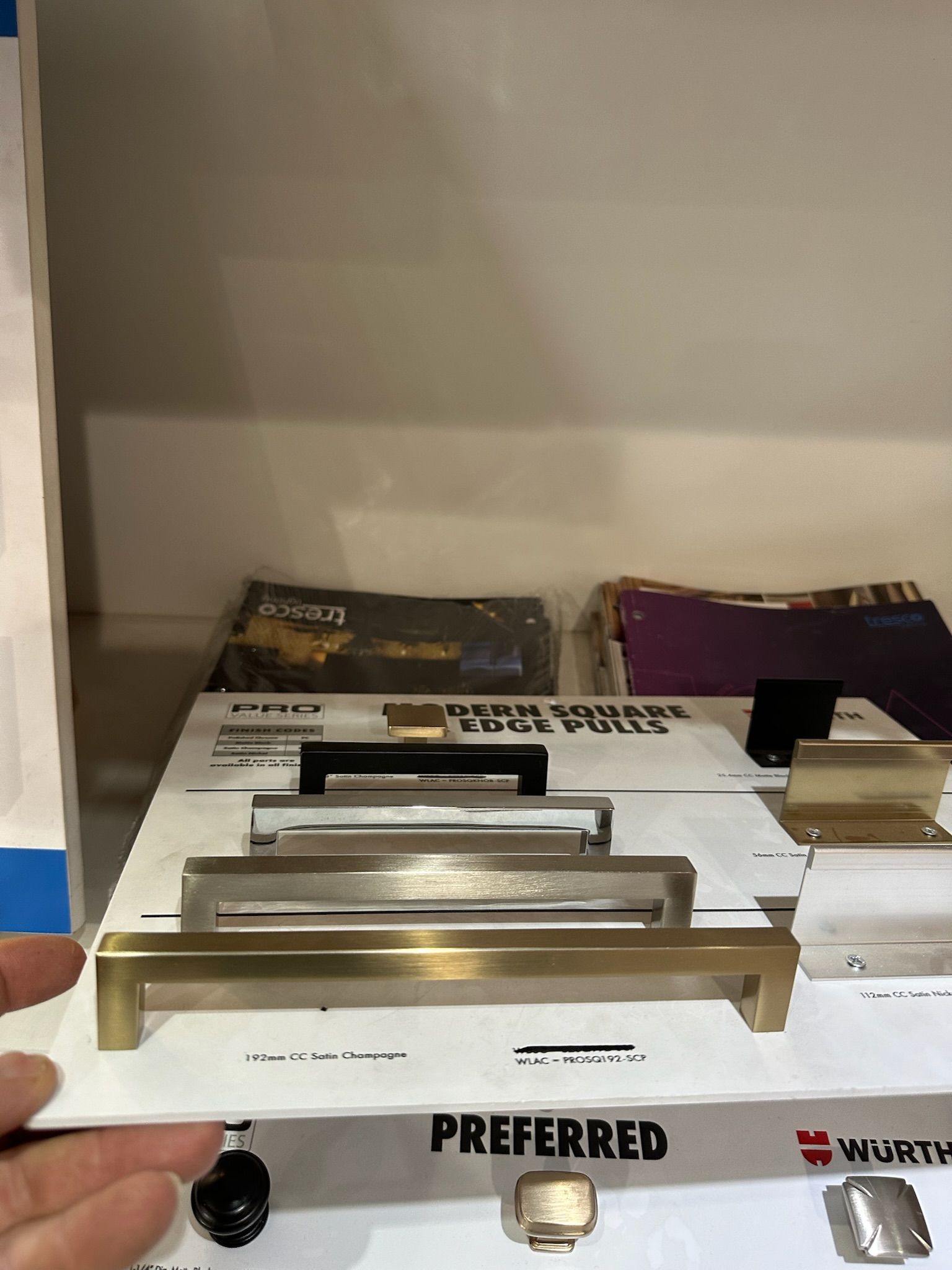 A hand holds a display of cabinet pulls in various metallic finishes.