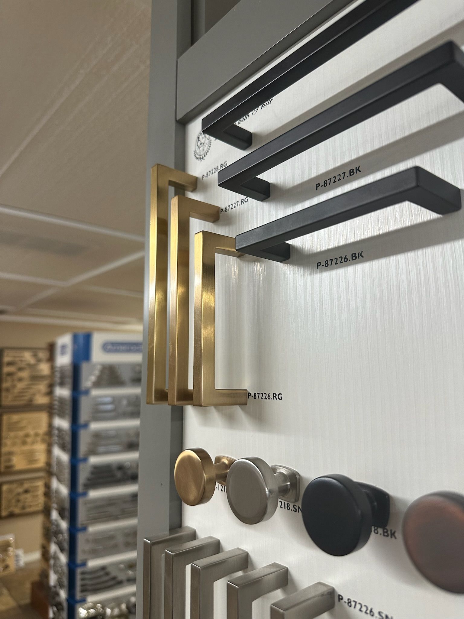 Cabinet hardware display: gold and black pull handles, round knobs in various metallic finishes.
