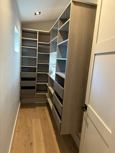 Walk-in closet with light wood flooring and built-in shelving, drawers, and storage.