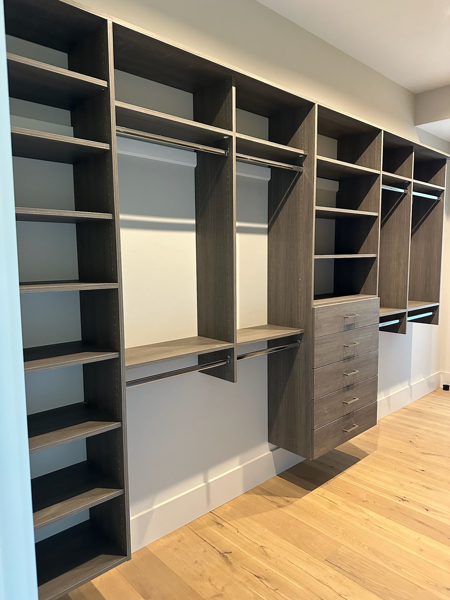 Built-in closet with dark gray shelves, rods, and drawers against a light-colored wall and wood floor.