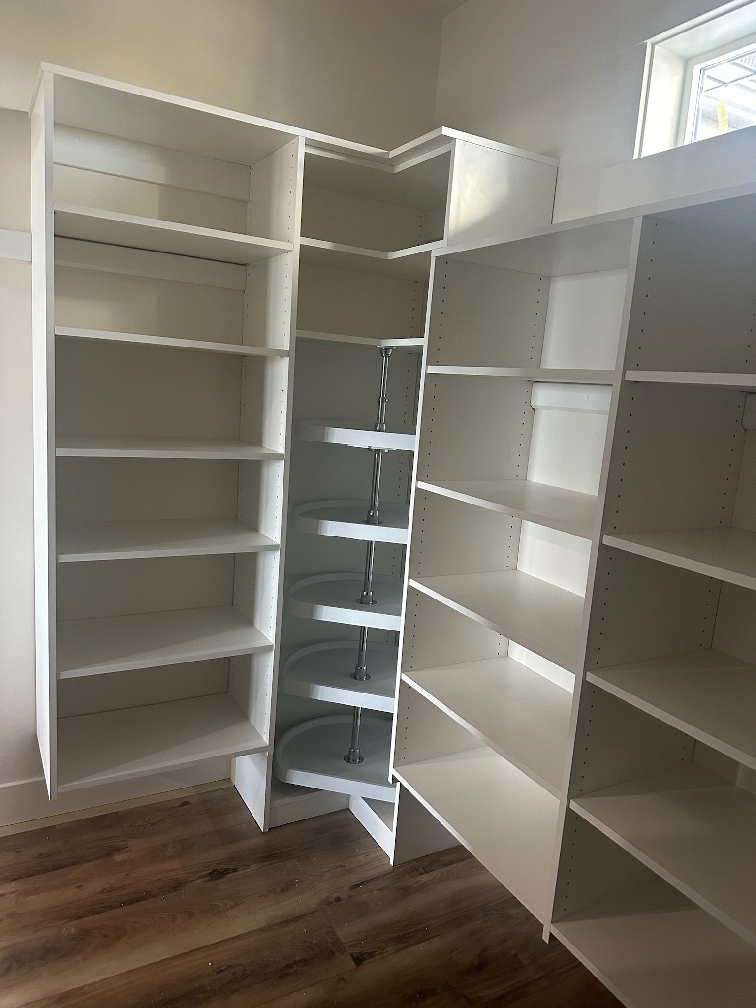 White corner cabinet with many shelves, set against wooden floor.