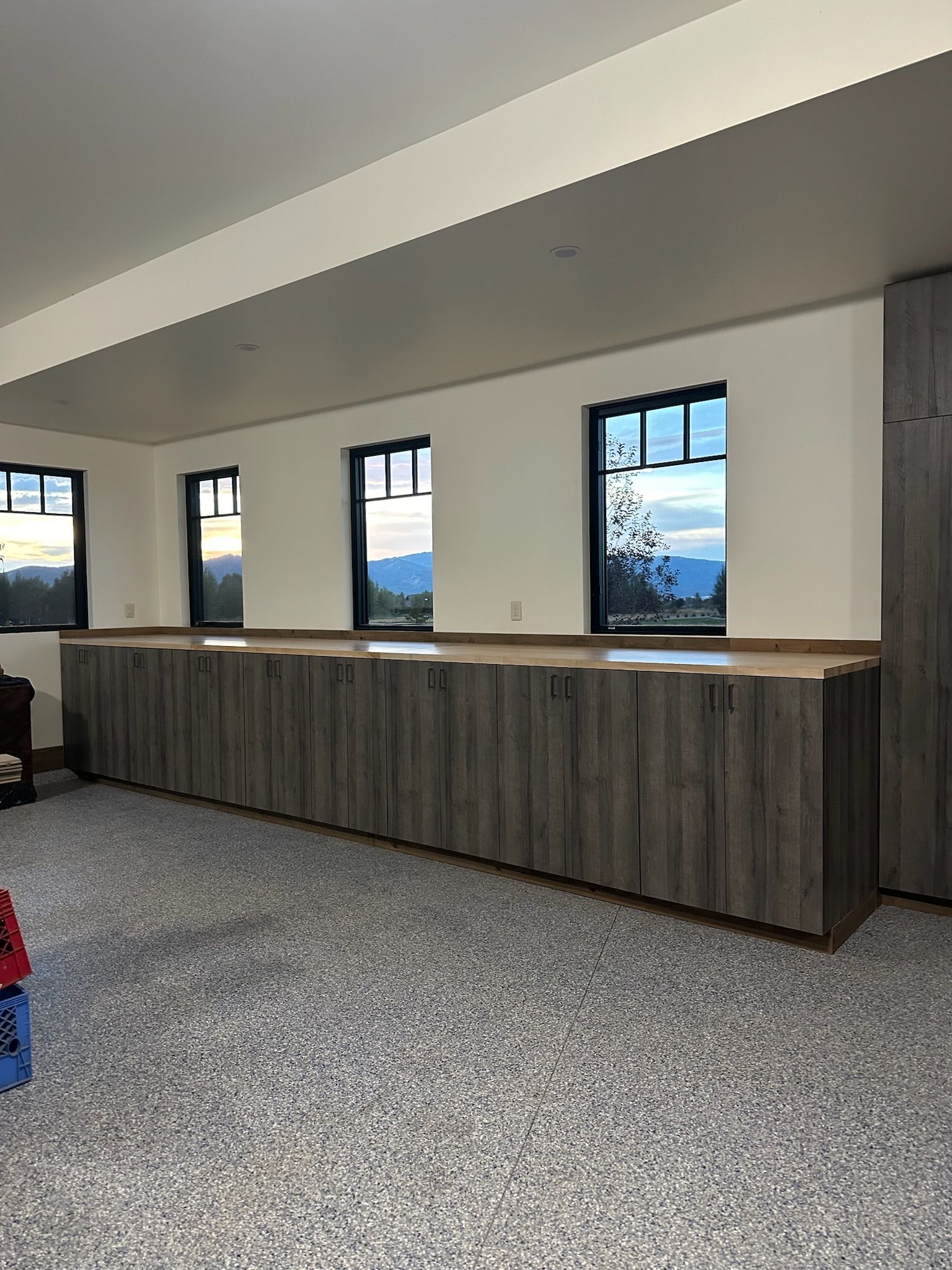 Long row of gray cabinets under windows in a room with a speckled floor.
