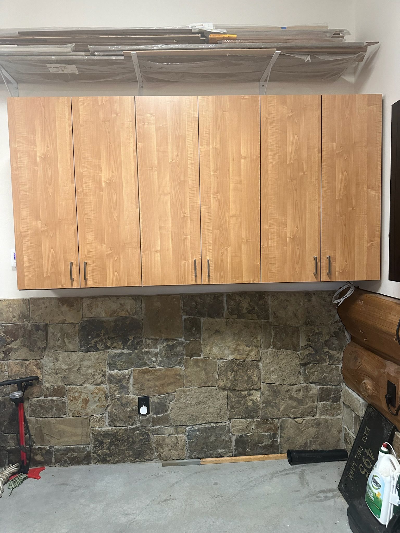 Wooden cabinets mounted on a wall above a stone wall, garage interior.