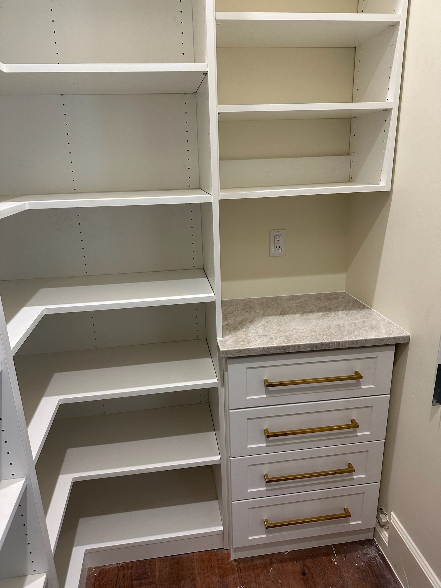 White pantry with built-in shelves and drawers, topped with a stone counter. Gold handles on drawers.
