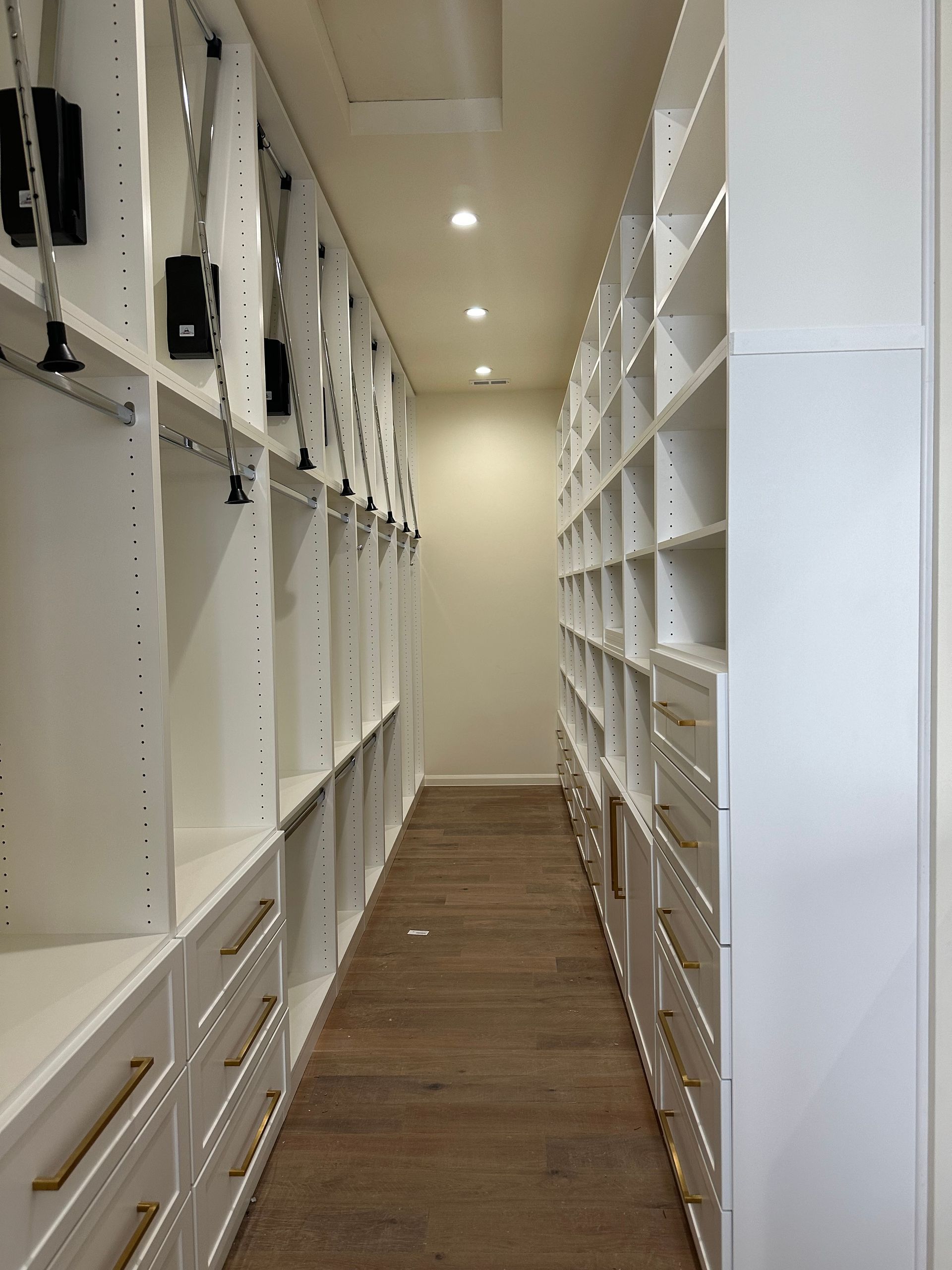 Narrow white closet with drawers and shelves, wooden floor.