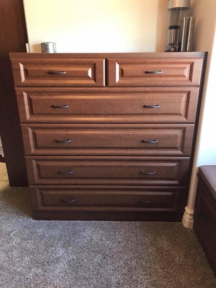 Brown wooden dresser with five drawers and dark handles, in a room with carpet.