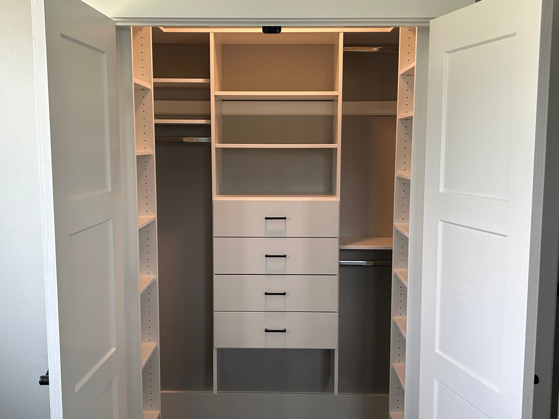 White built-in closet with shelves, drawers, and hanging rods. Open doors frame the interior.