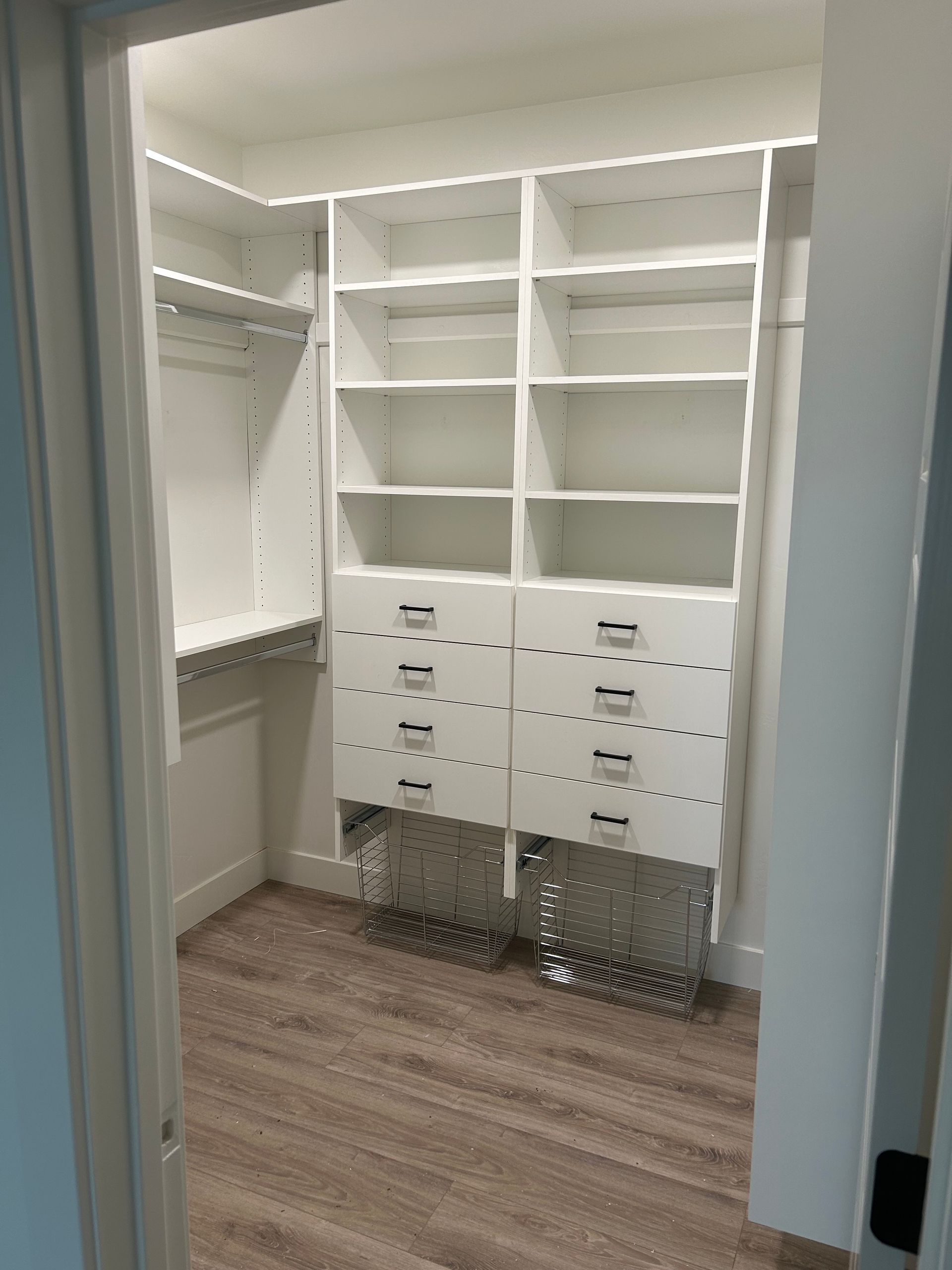 White walk-in closet with shelves, drawers, and clothing rods; light brown floor.