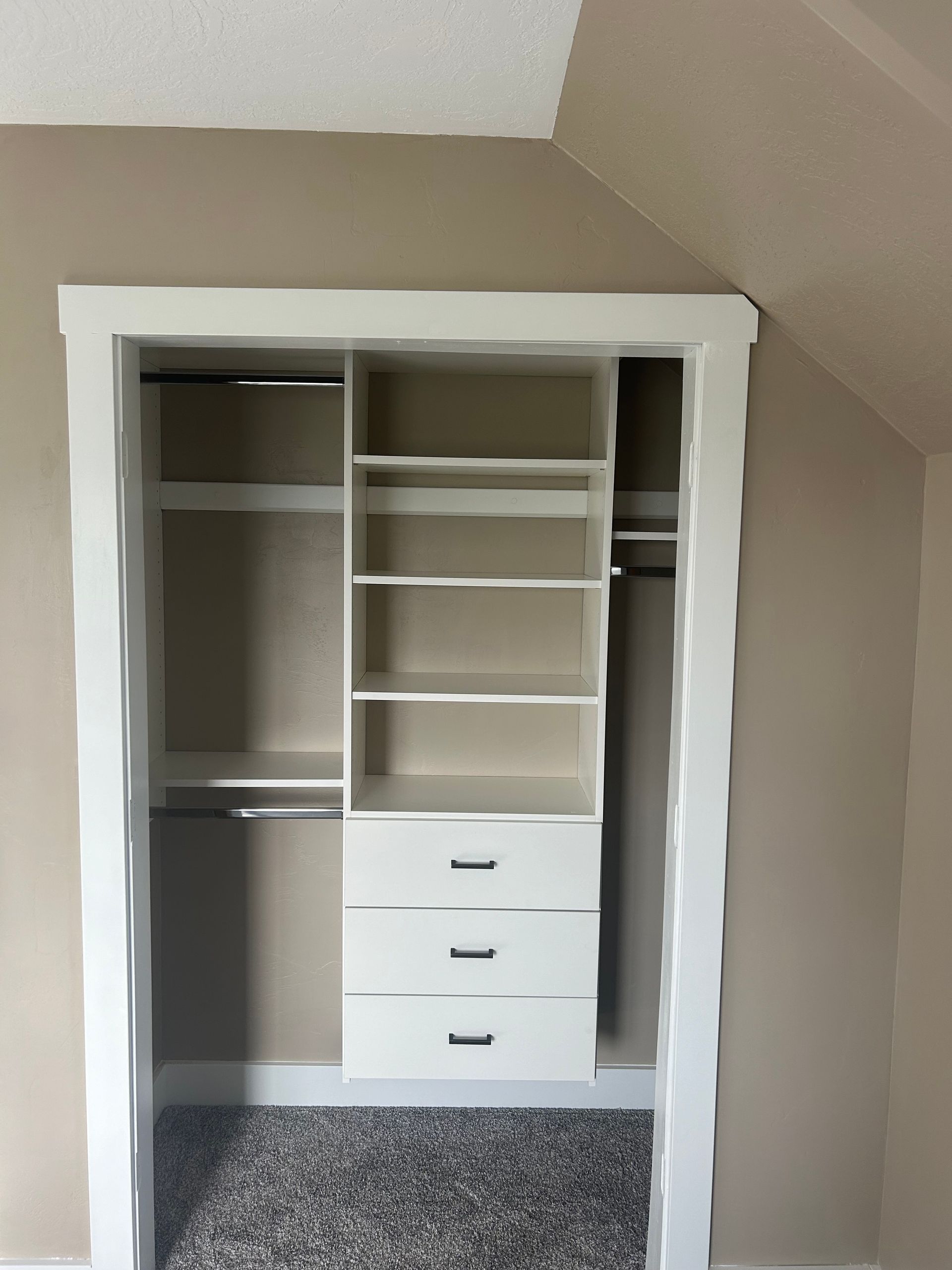 White built-in closet with shelves, drawers, and hanging rods inside a room with beige walls.