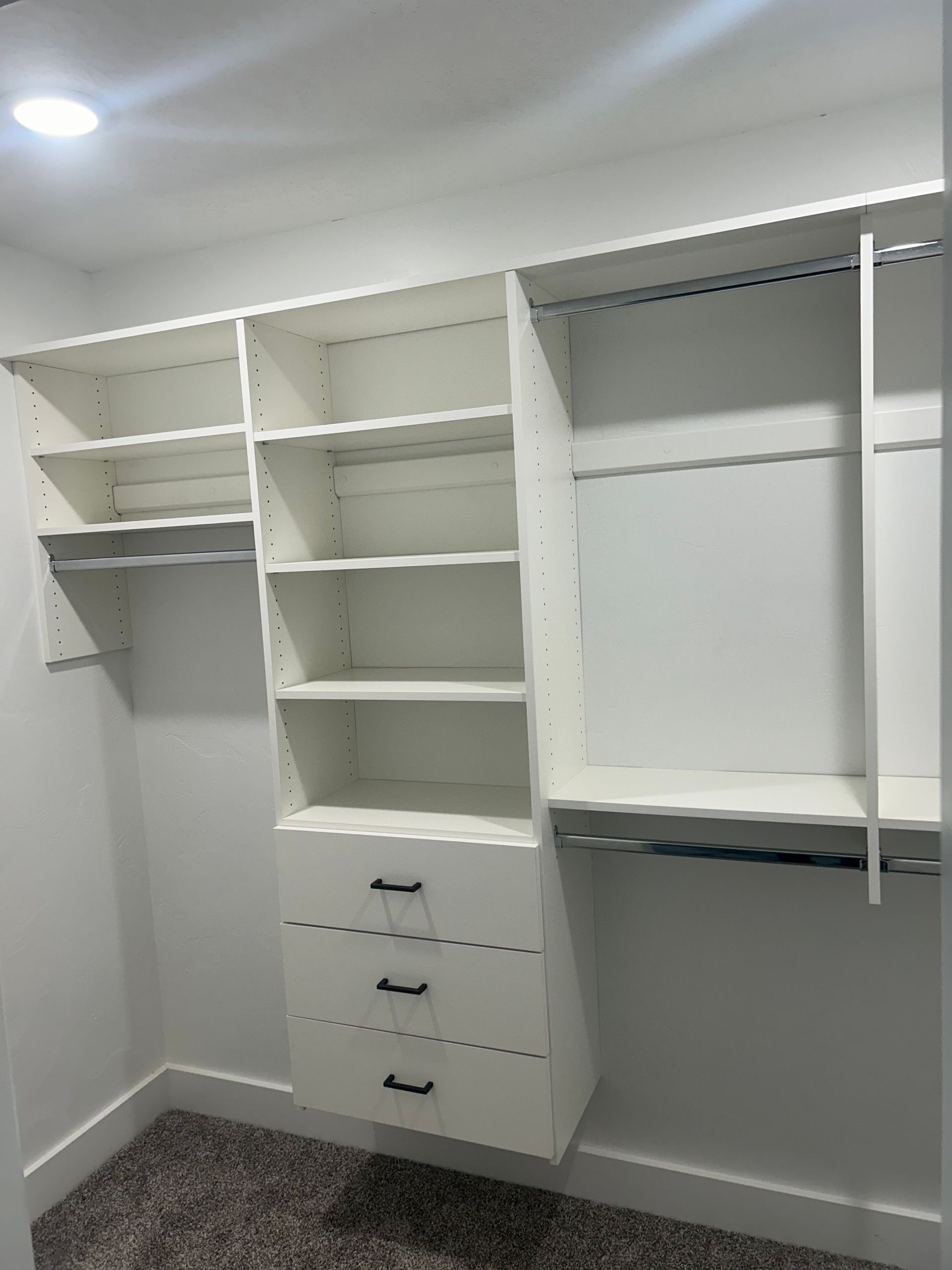 White closet organization system with shelves, drawers, and hanging rods in a corner.