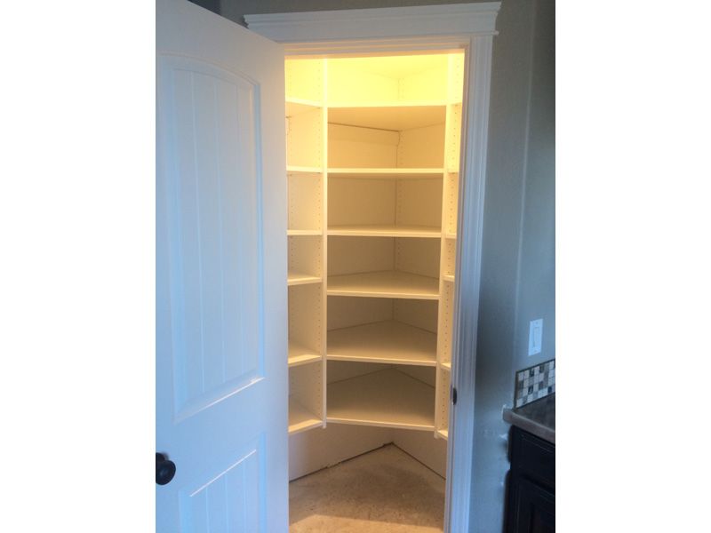 A white pantry with built-in shelves is open, showing neat storage, with a door ajar and dim lighting.