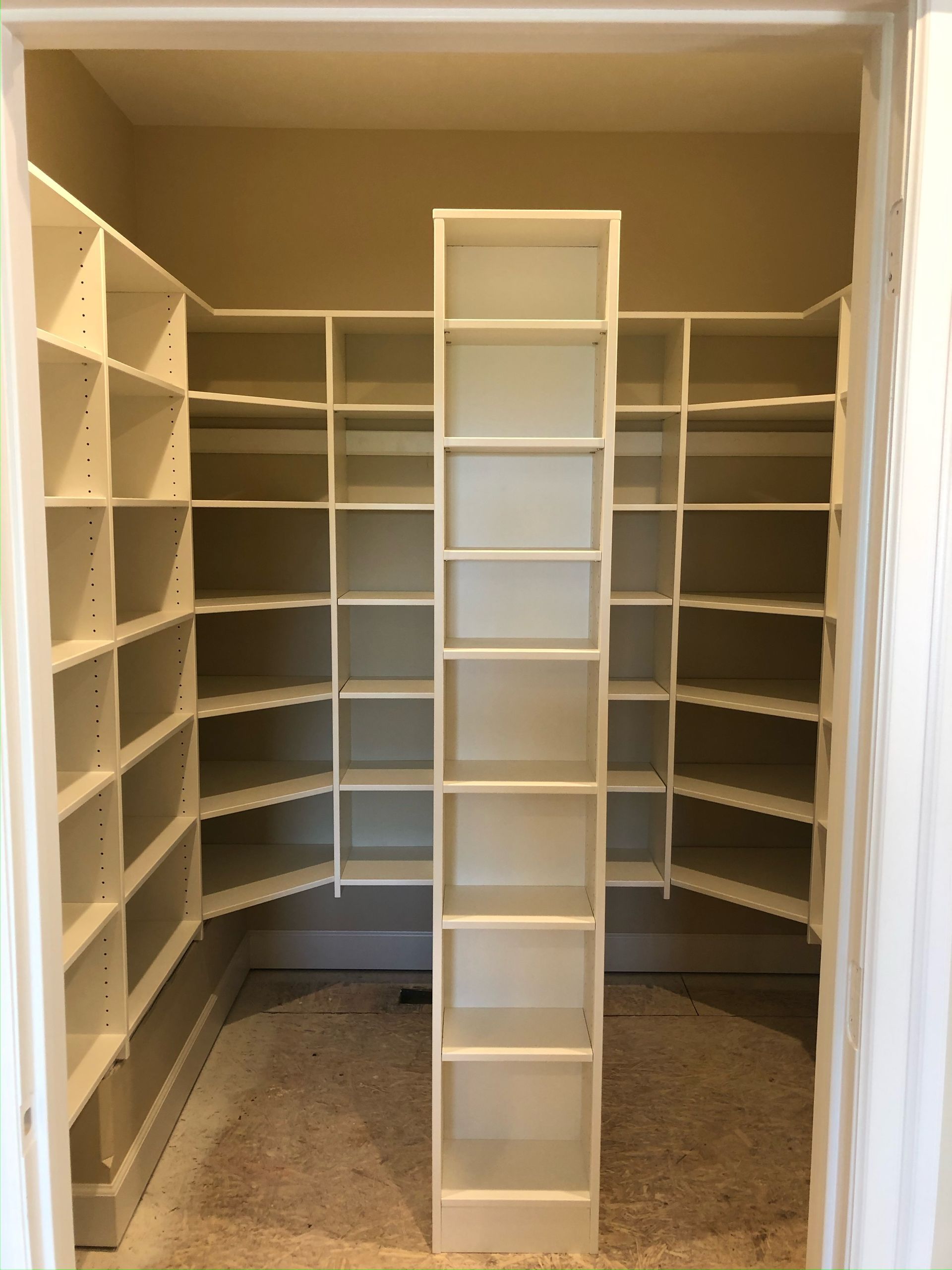 Empty built-in closet with white shelving. A central tower separates two angled shelving units. Beige walls.
