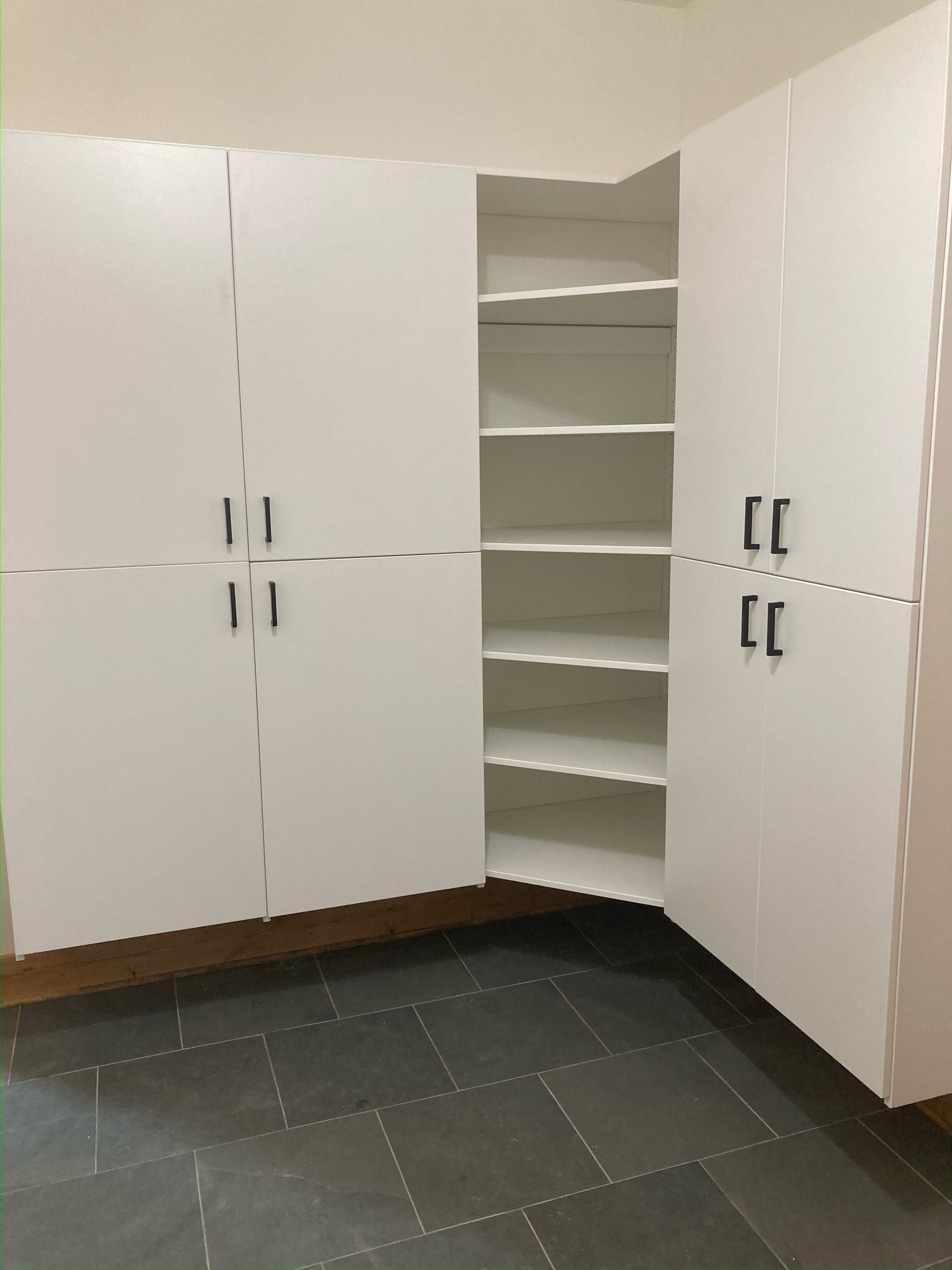 White storage cabinets in a corner of a room, one cabinet open showing shelves.