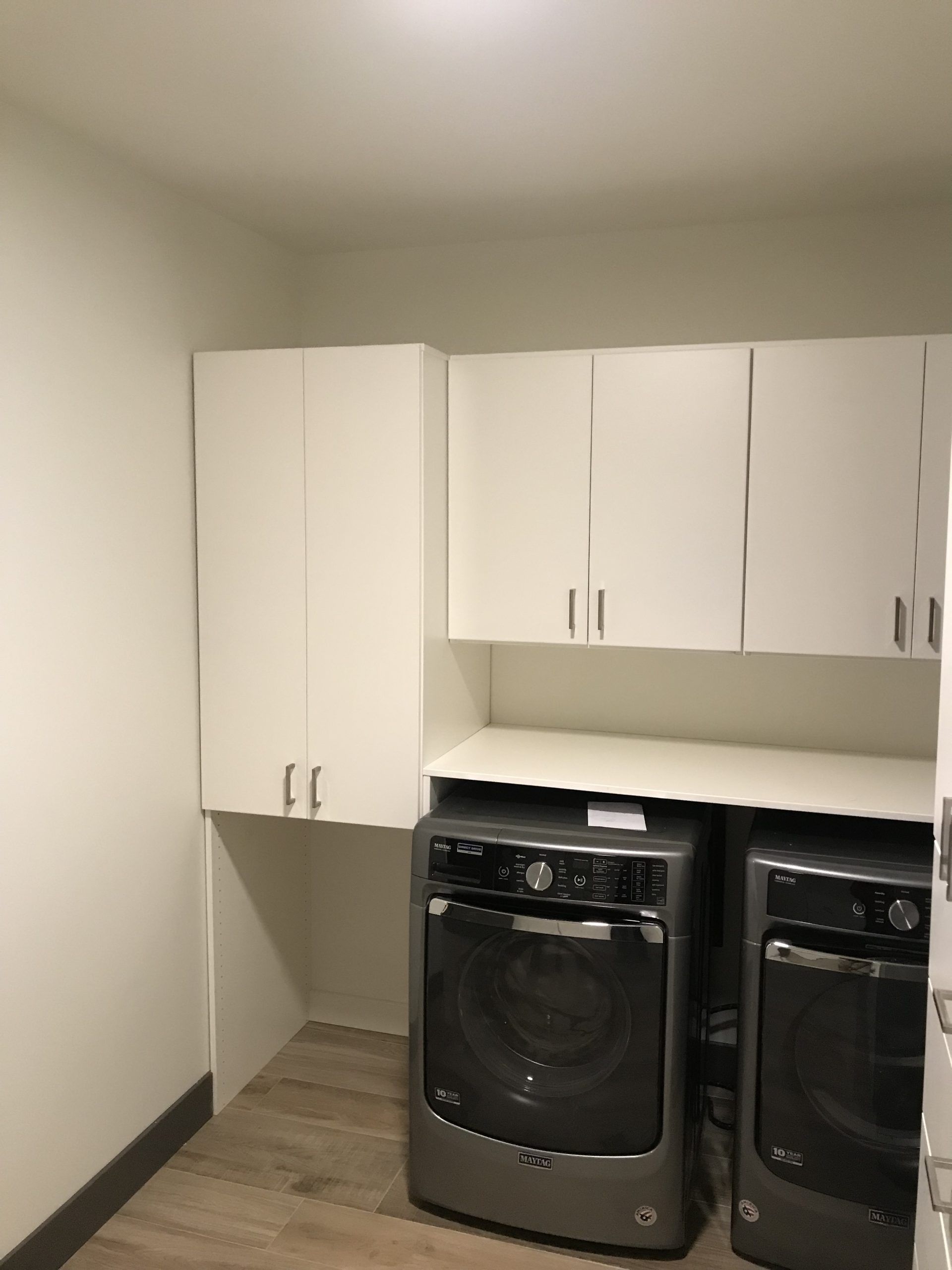 Laundry room with white cabinets, washer, dryer, and light-colored wood-look flooring.