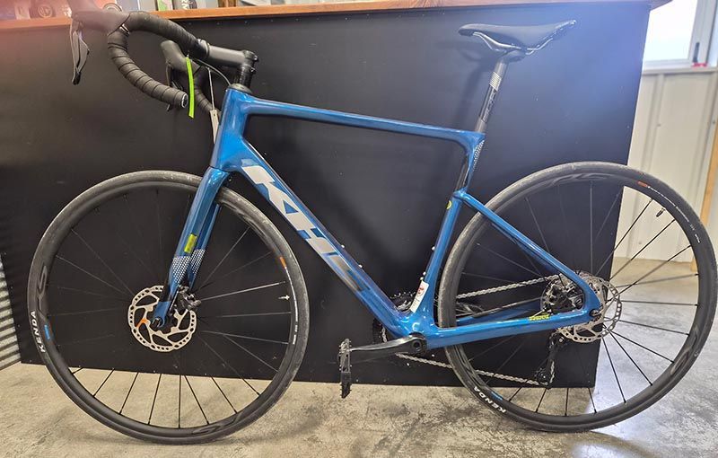 A blue KHS gravel bike with disc brakes and drop handlebars, positioned against a dark counter.