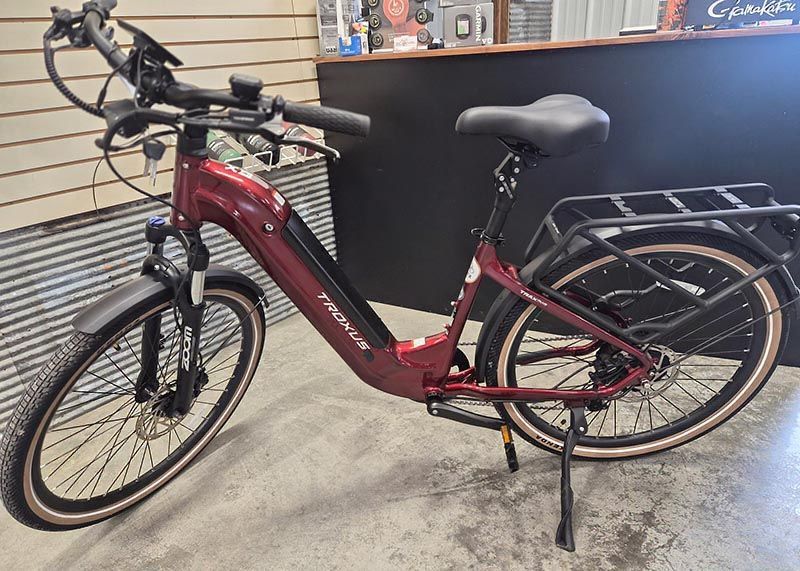 A dark red step-through electric bicycle with a rear cargo rack and suspension fork parked indoors.
