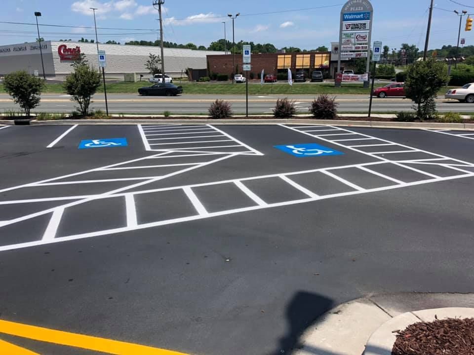 Two blue handicap parking space symbols painted on black asphalt with white-striped safety zones in a parking lot.