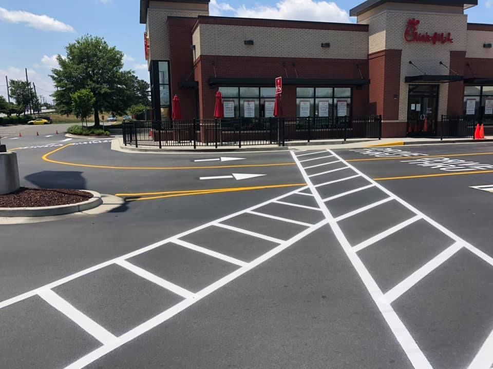 A Chick-fil-A restaurant with a drive-thru lane marked by white painted road lines and directional arrows on the asphalt.